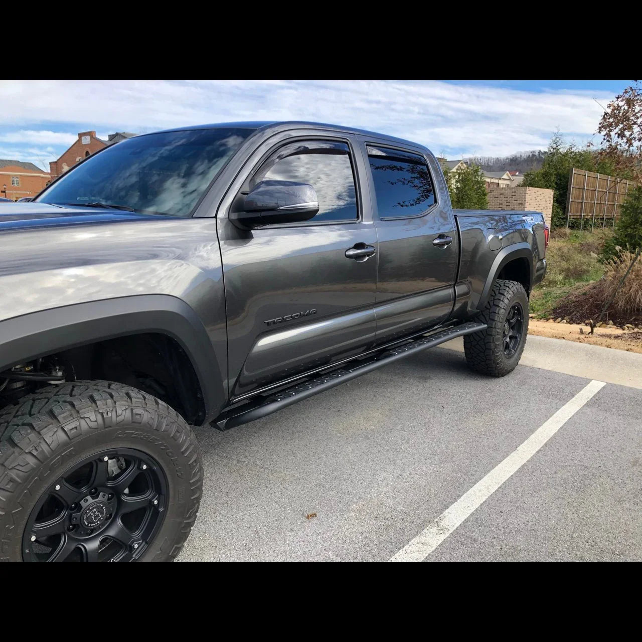Toyota Tacoma with black off-road wheels and side step parked outdoors
