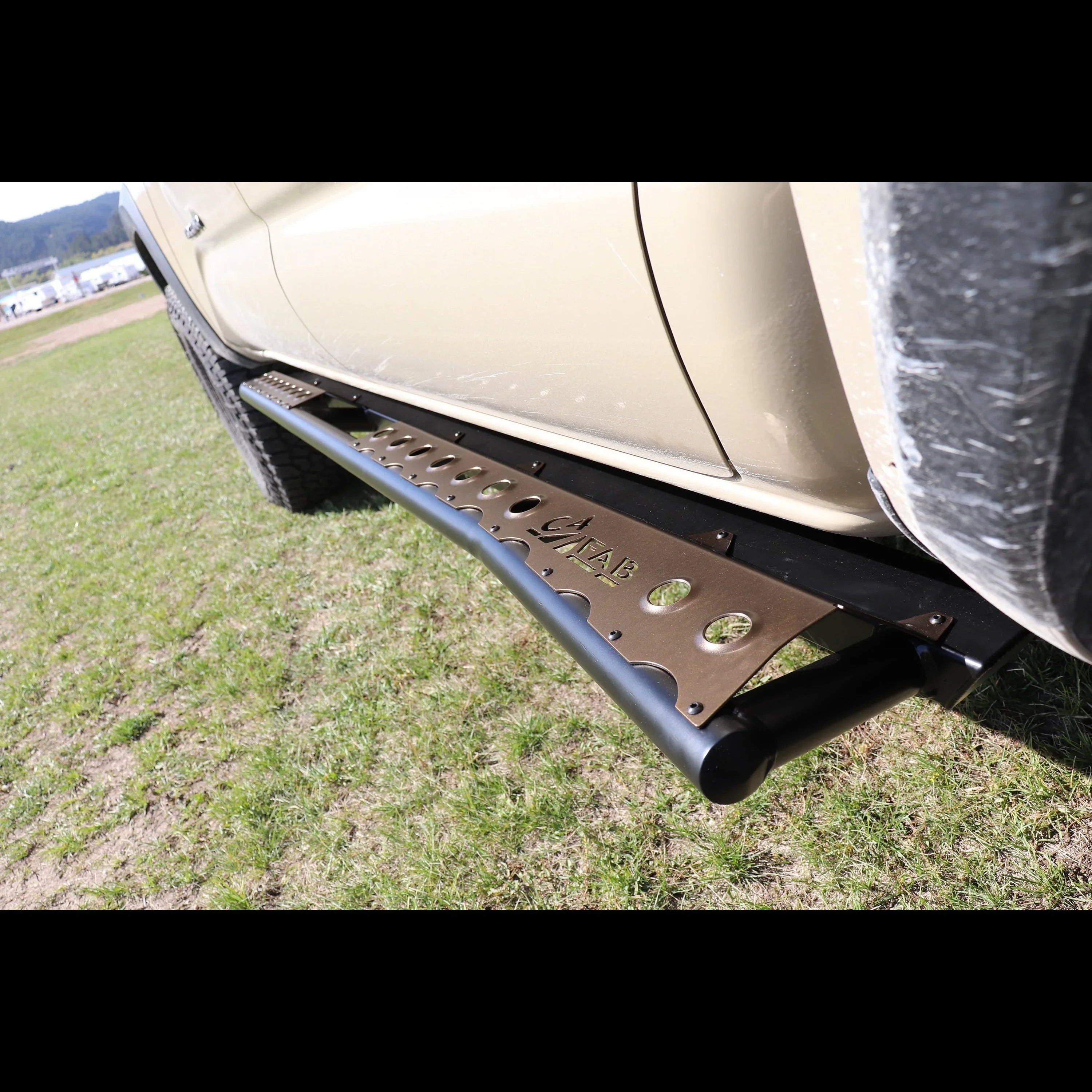 Off-road rock slider with metal step mounted on beige truck in grassy outdoor setting