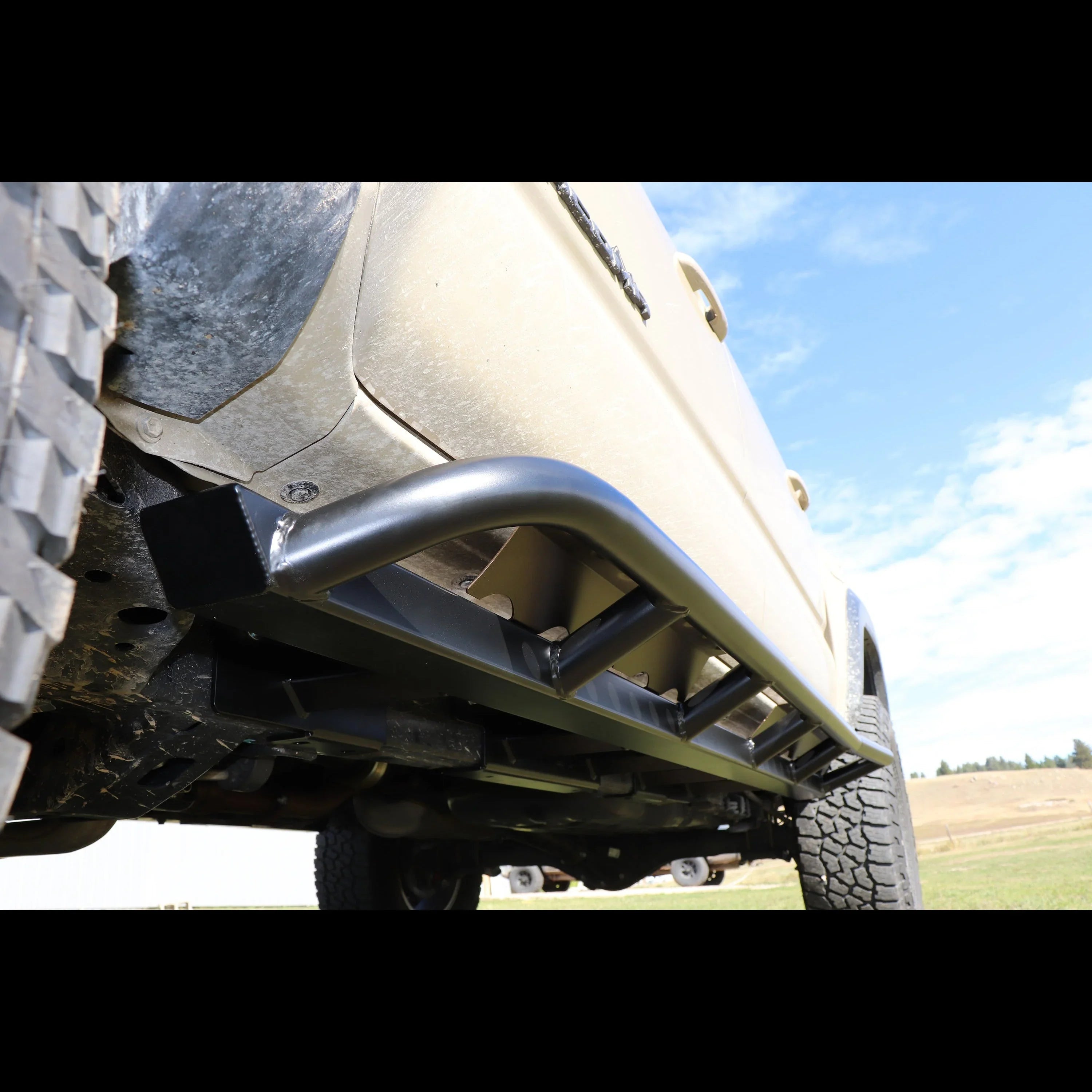 Black off-road rock sliders installed on a beige Toyota pickup truck in outdoor setting