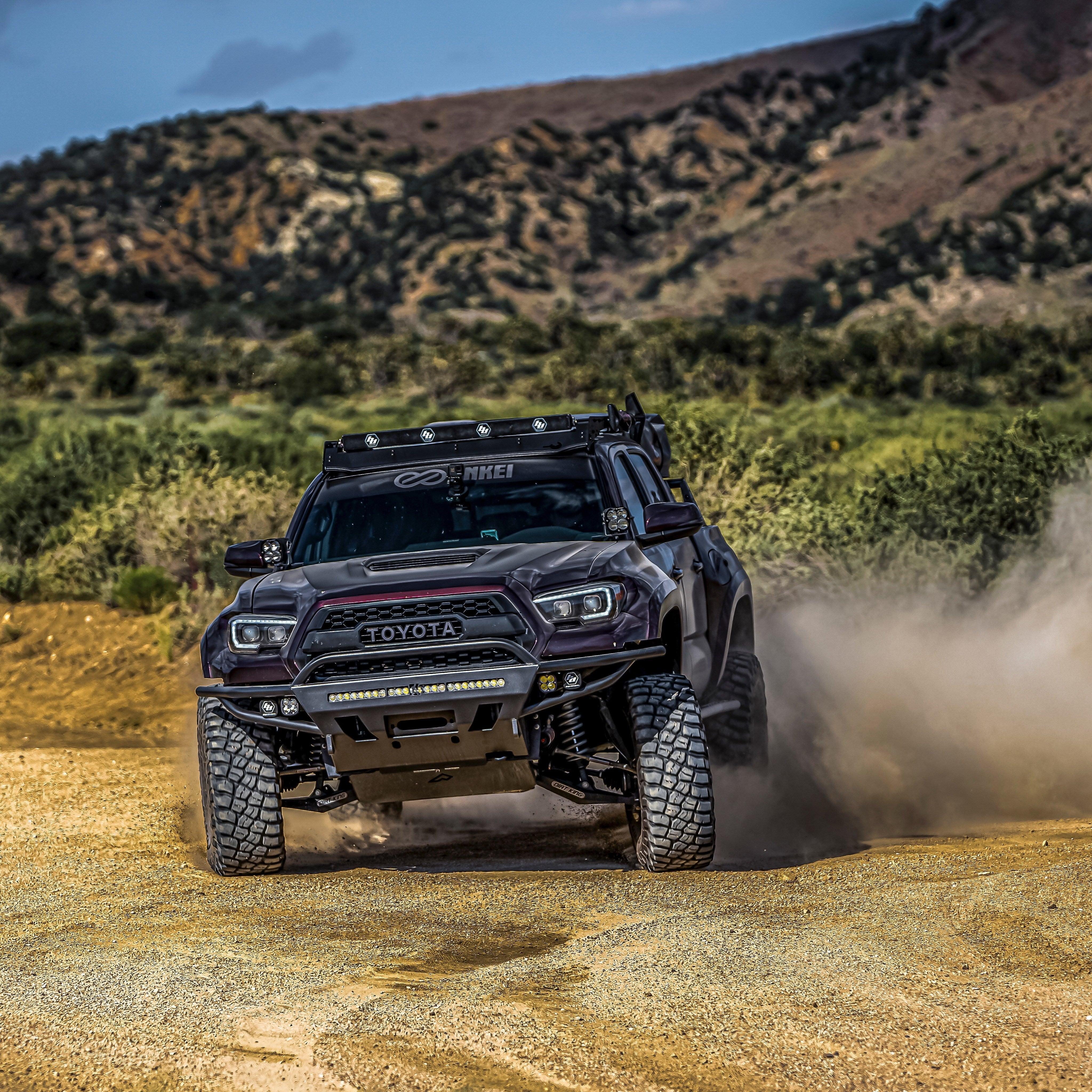 Lifted Toyota Tacoma off-road truck driving on dusty trail with rugged terrain and mountains