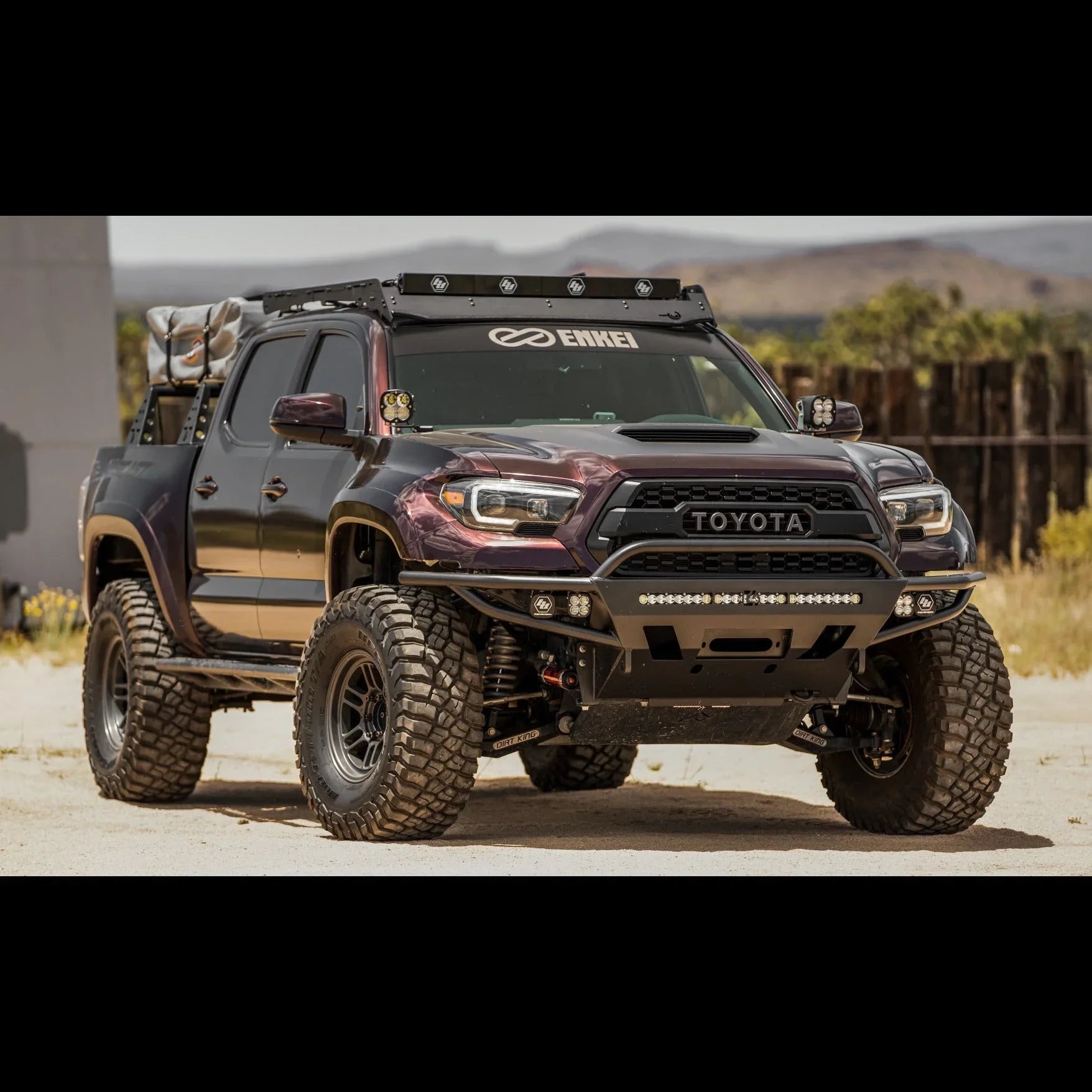 Lifted Toyota Tacoma with off-road tires, roof rack, lights, and overlanding gear in desert