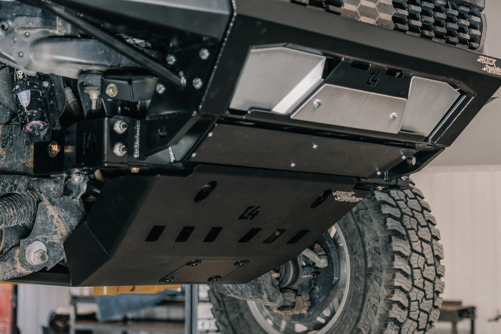 Heavy-duty off-road skid plate installed under a lifted truck, showing rugged suspension and protective metal armor.