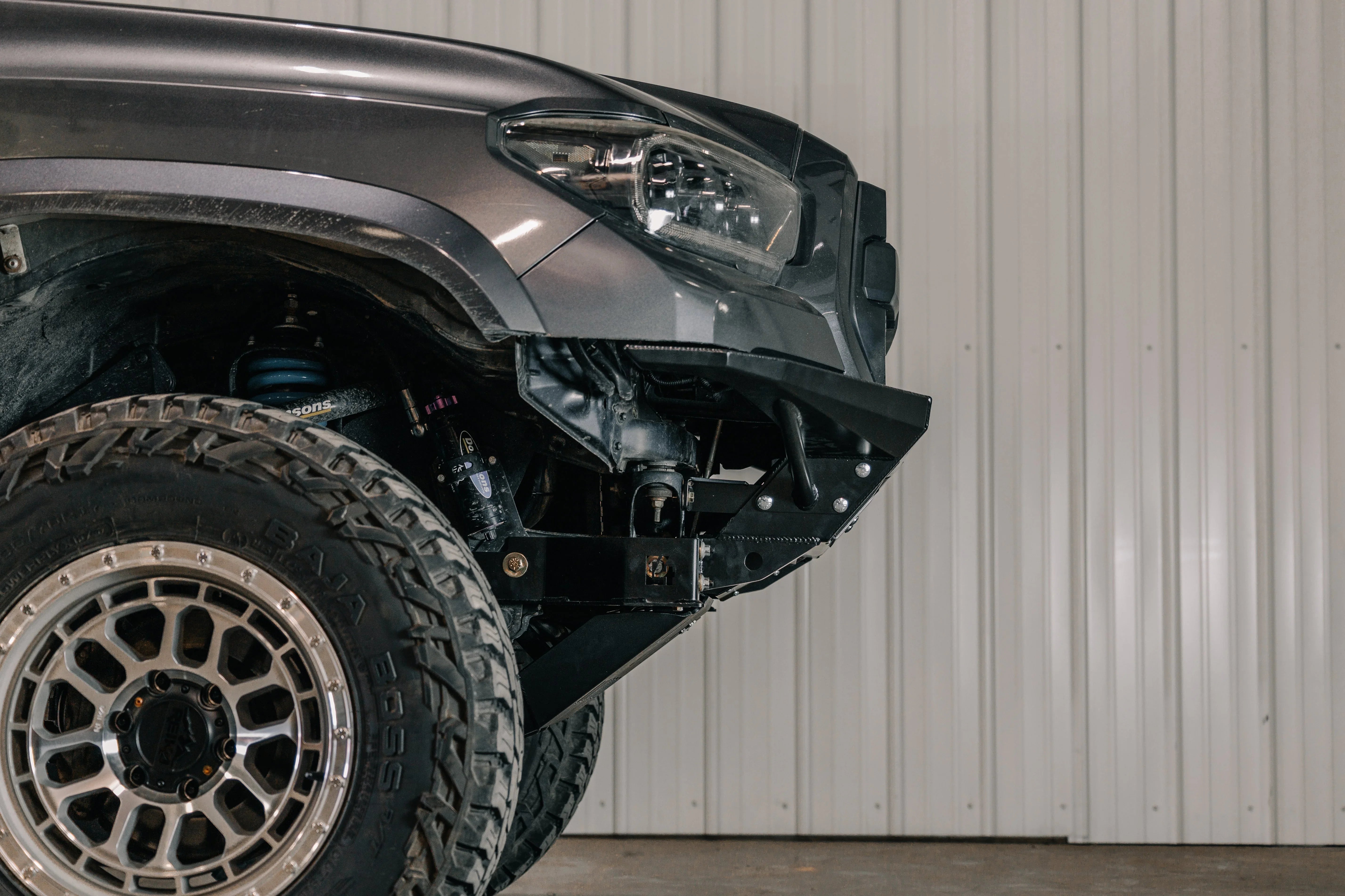 Toyota Tacoma front end with off-road steel bumper and all-terrain tire in garage