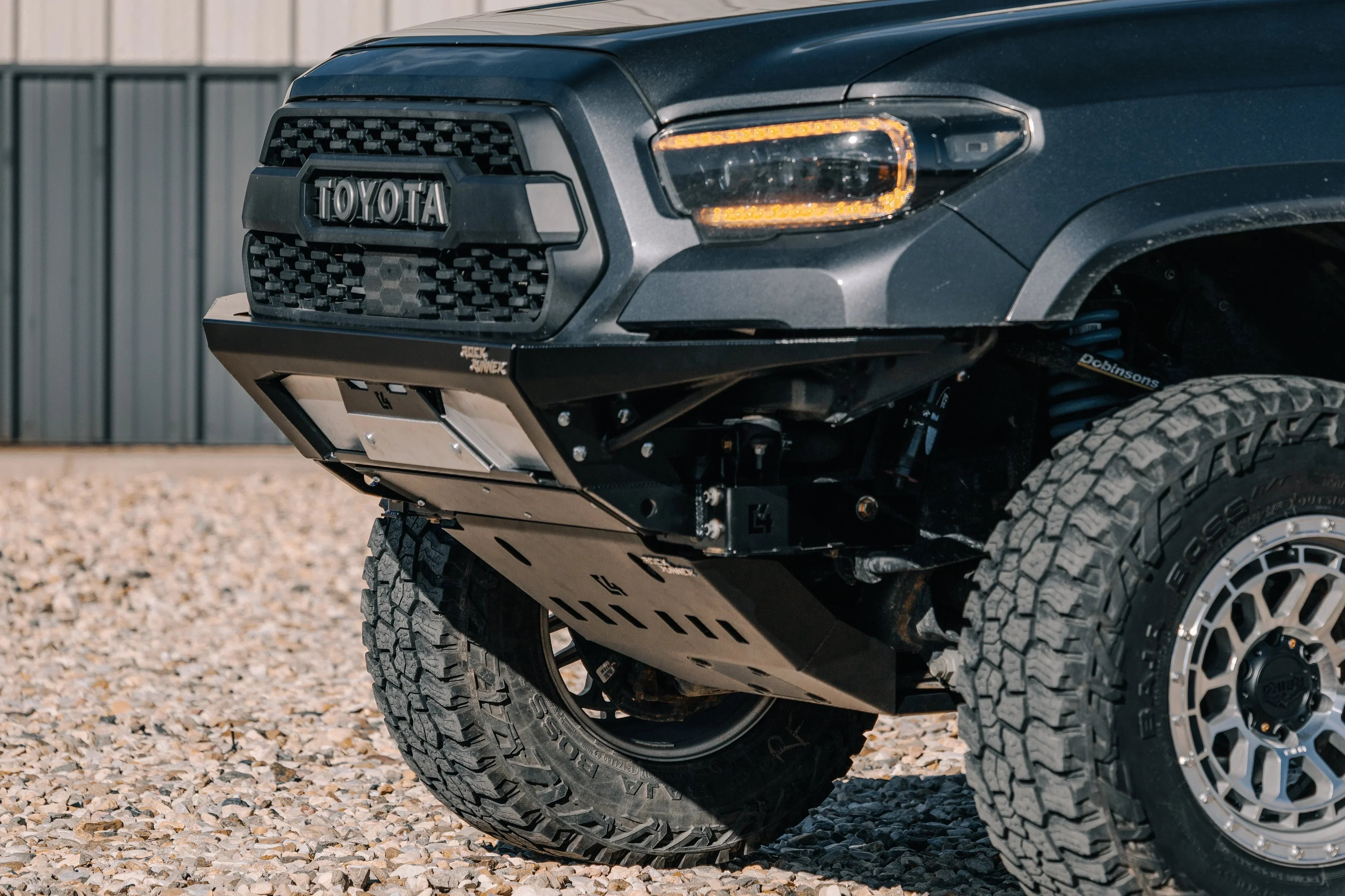 Toyota Tacoma front bumper with steel skid plate and off-road tires on gravel