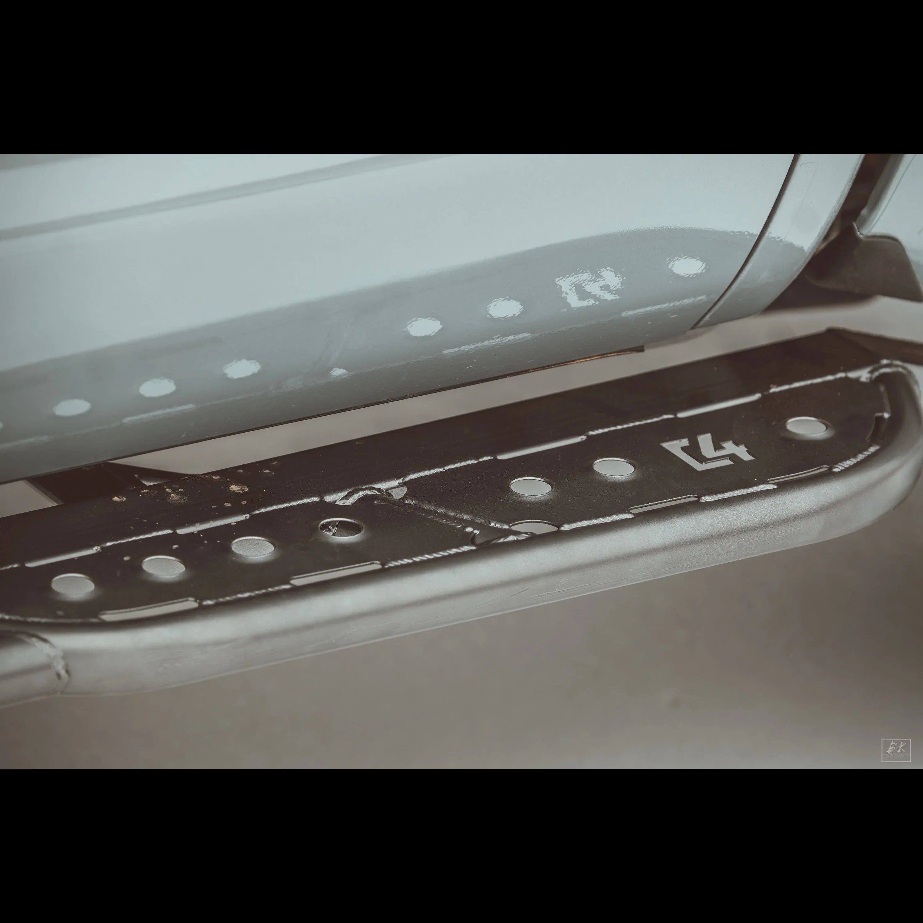 Close-up of metal rock slider step for off-road vehicle, black with C4 logo and bolt details.