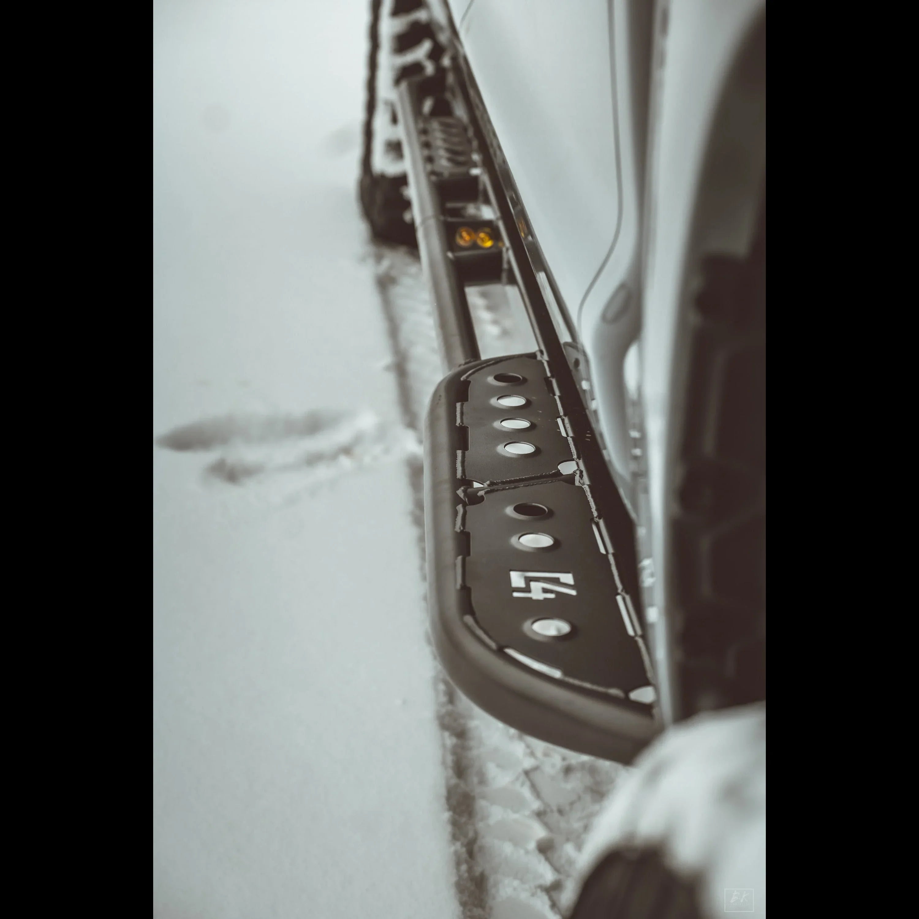 Close-up of a rugged off-road rock slider step attached to a vehicle in snowy conditions
