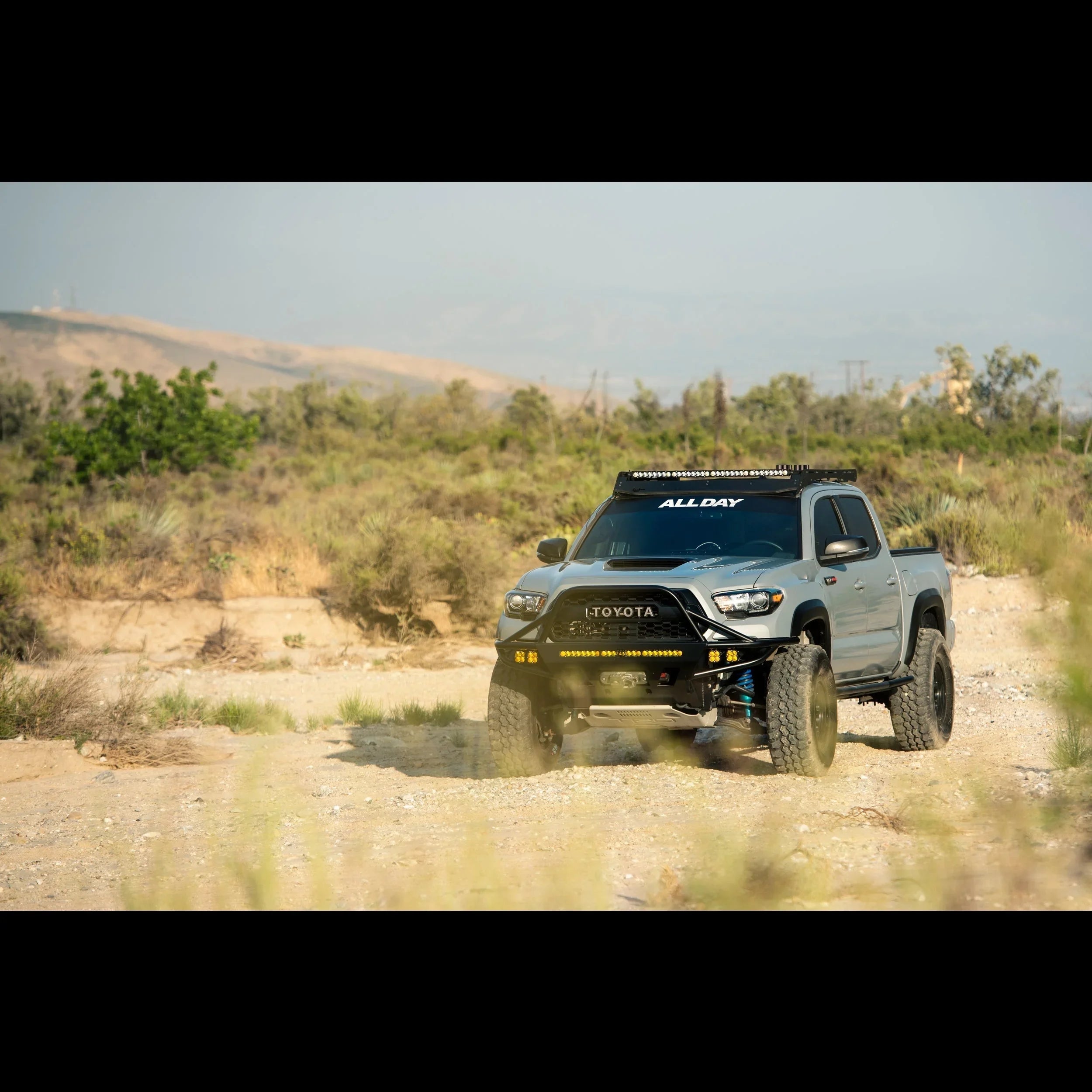 Lifted Toyota Tacoma off-road truck with aftermarket bumper and roof lights on dirt trail