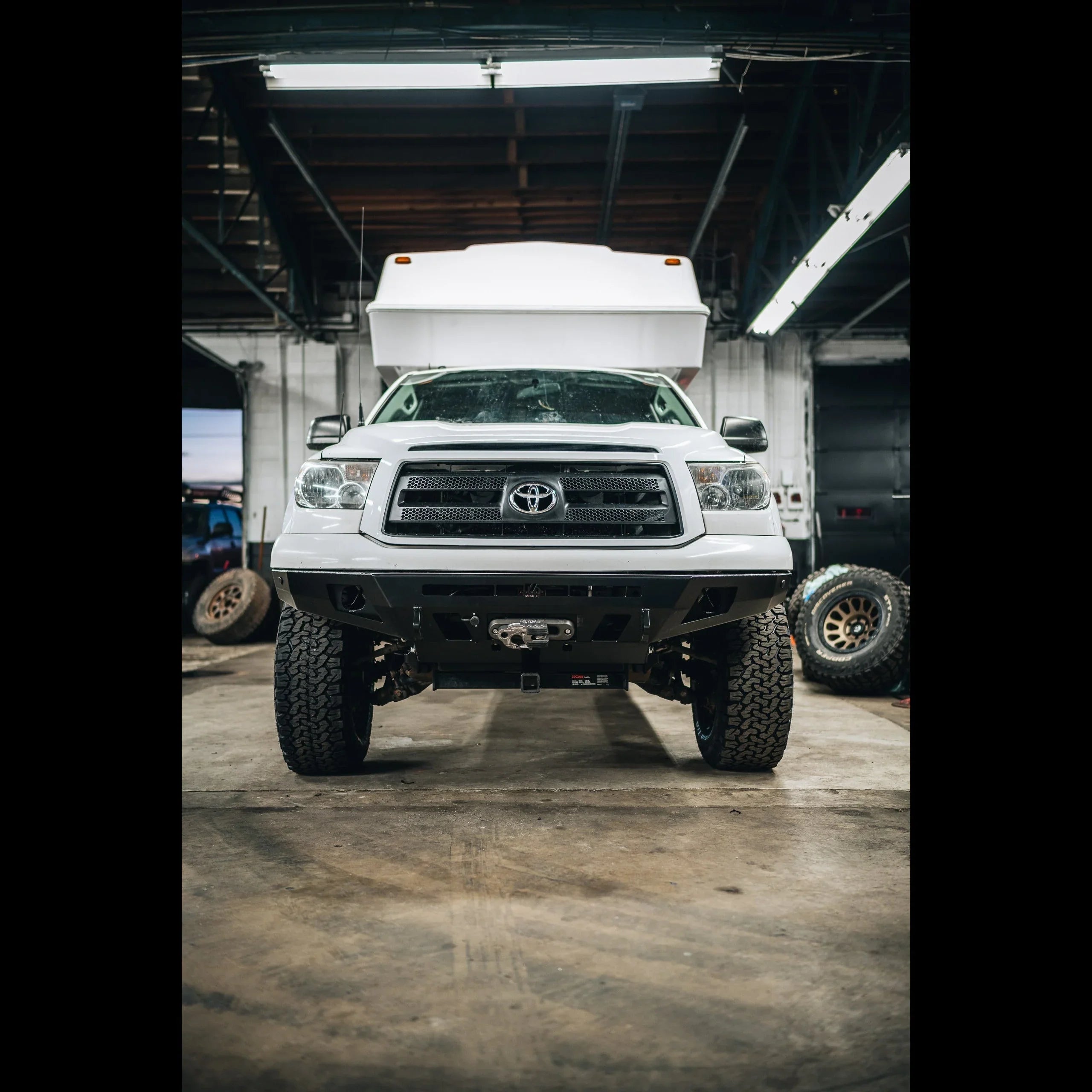 Front view of a white Toyota Tundra with off-road bumper and winch in a garage setting