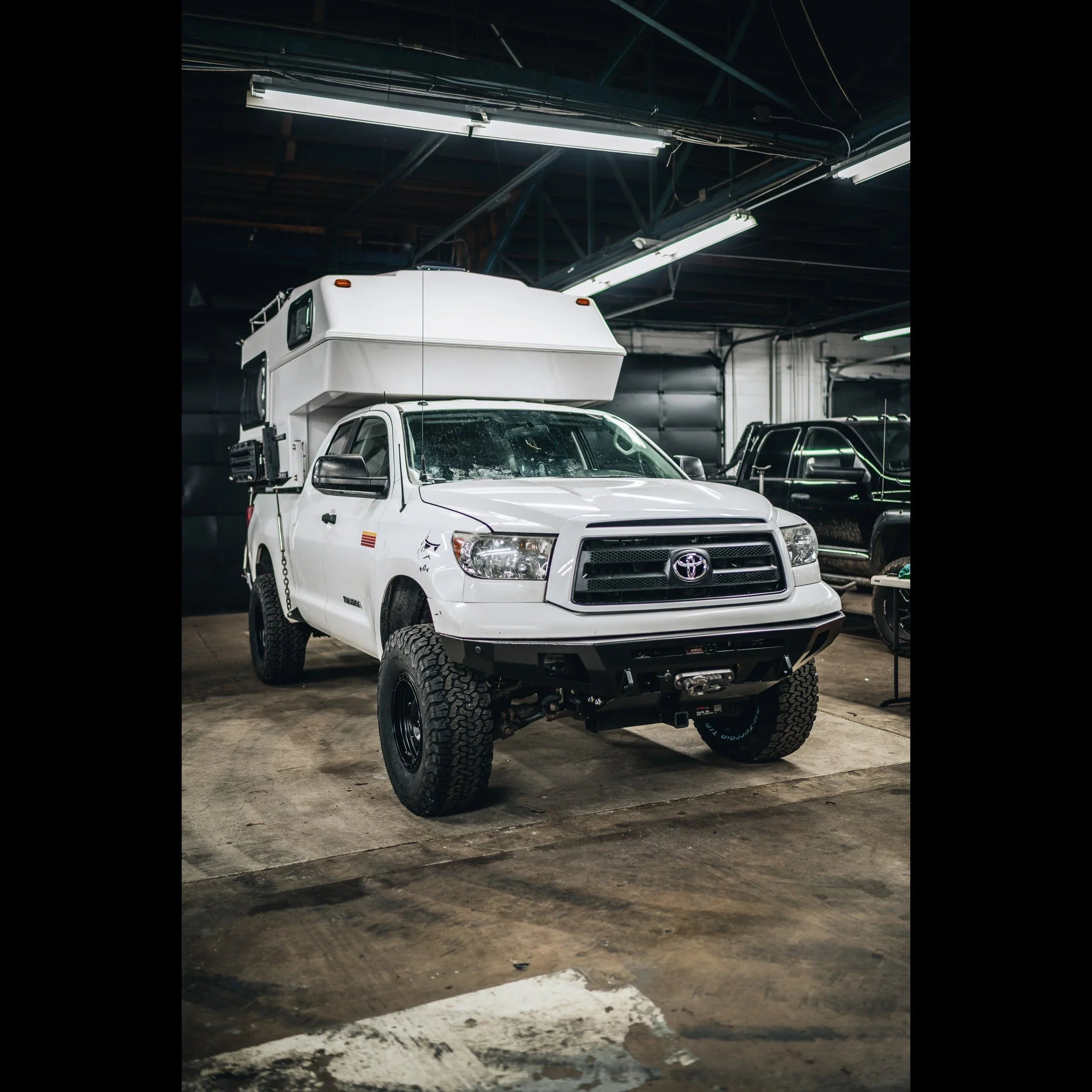 Lifted white Toyota Tundra with expedition camper parked indoors, overlanding setup