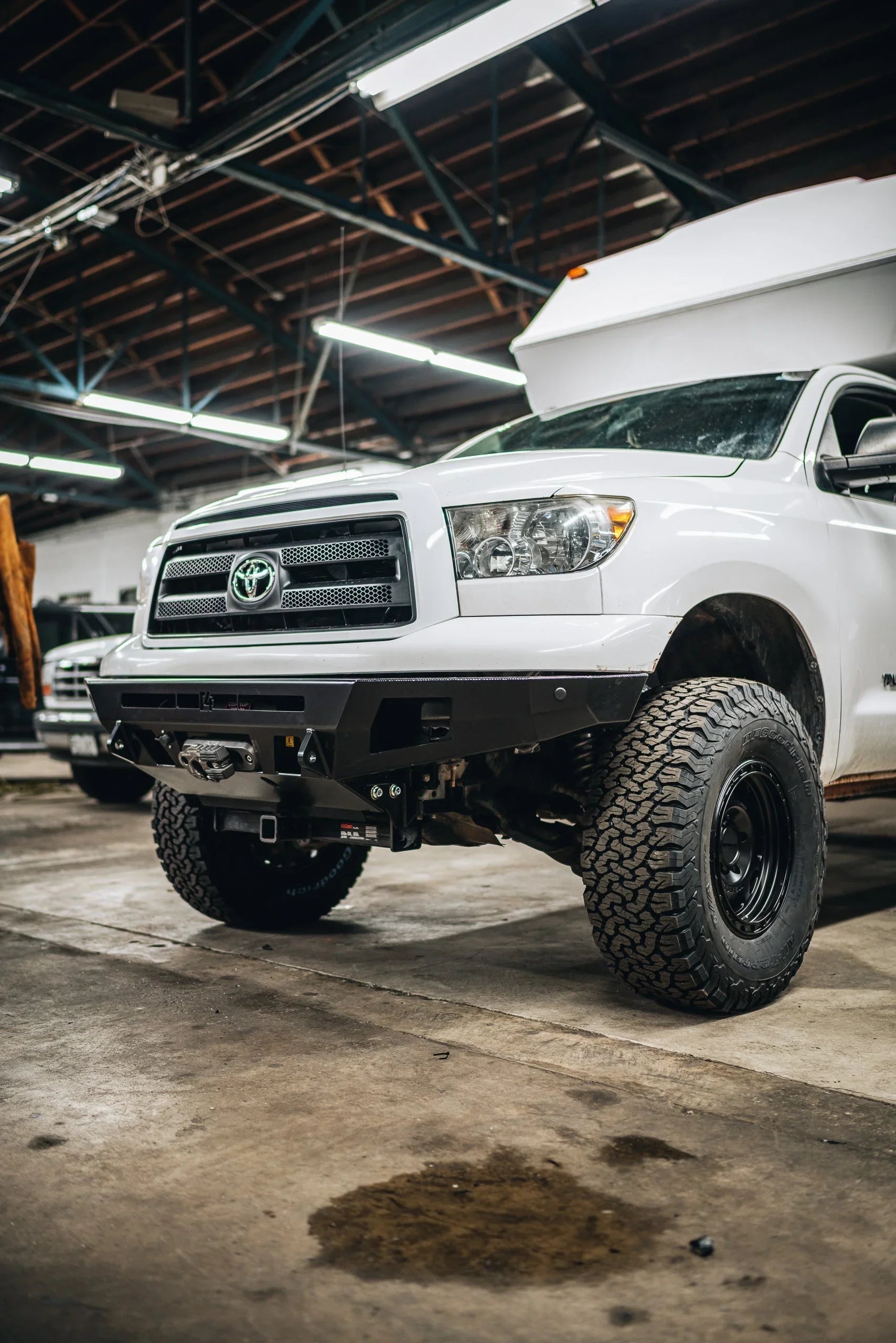 White Toyota Tundra with off-road bumper and all-terrain tires in a workshop setting