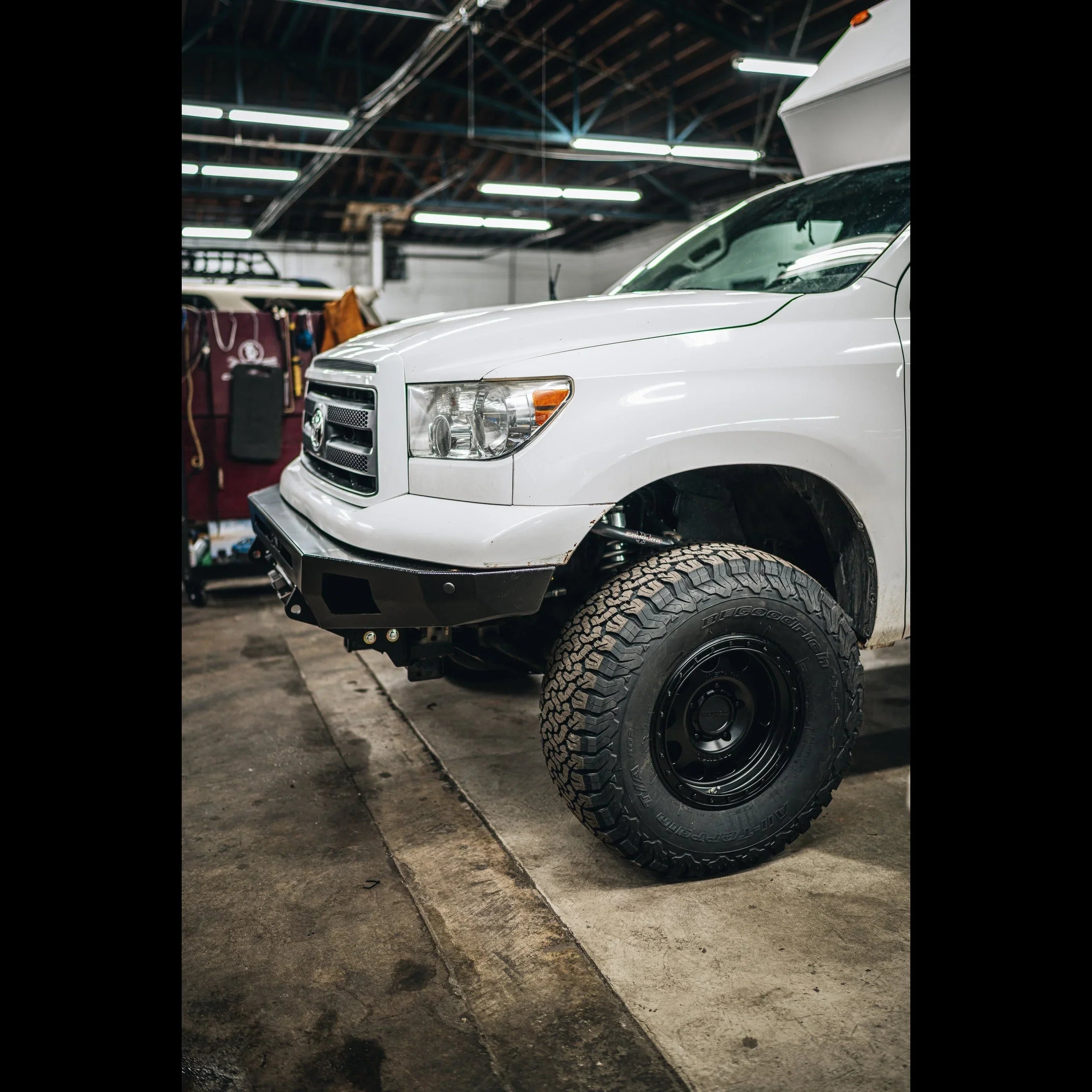 White Toyota Tundra with off-road bumper and all-terrain tires in a garage