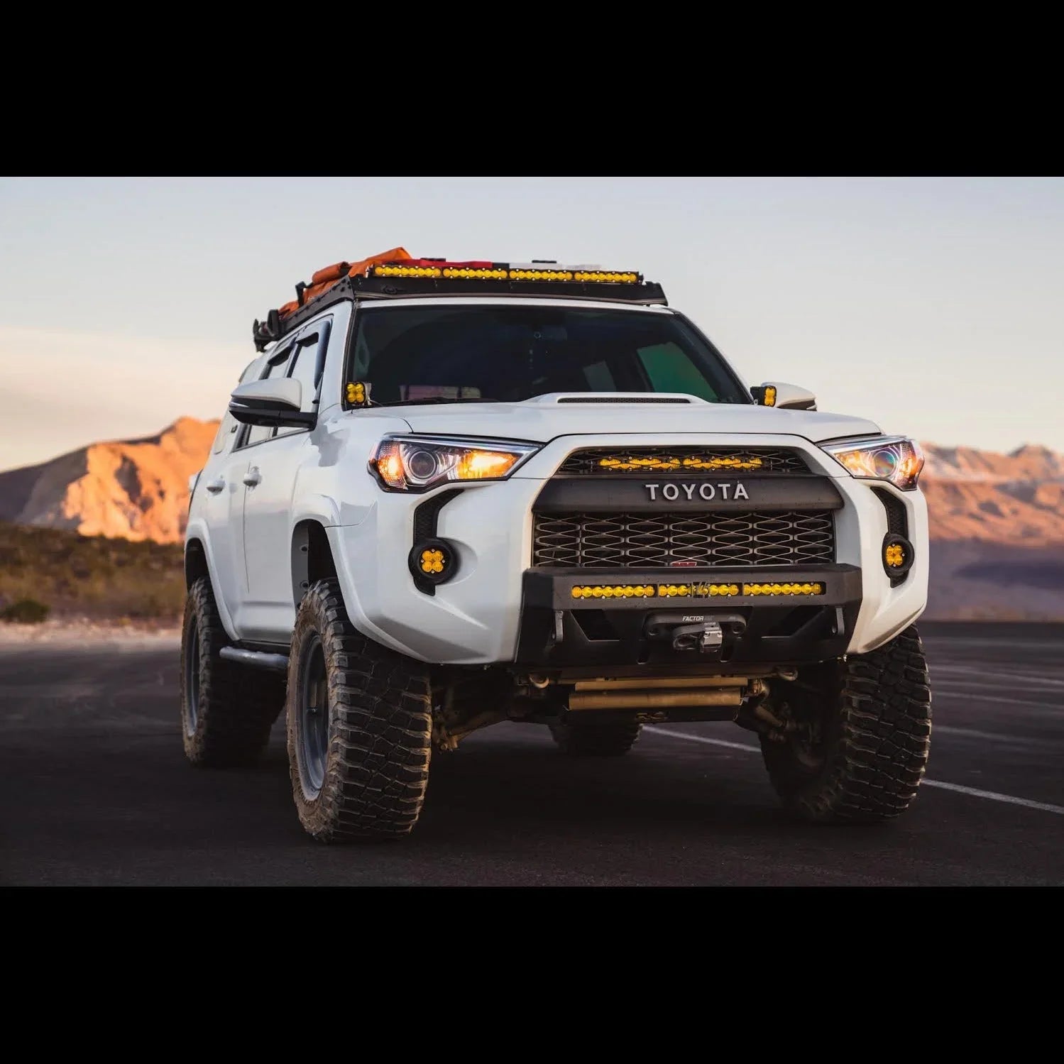 White Toyota 4Runner with off-road lights and roof rack parked in a desert landscape