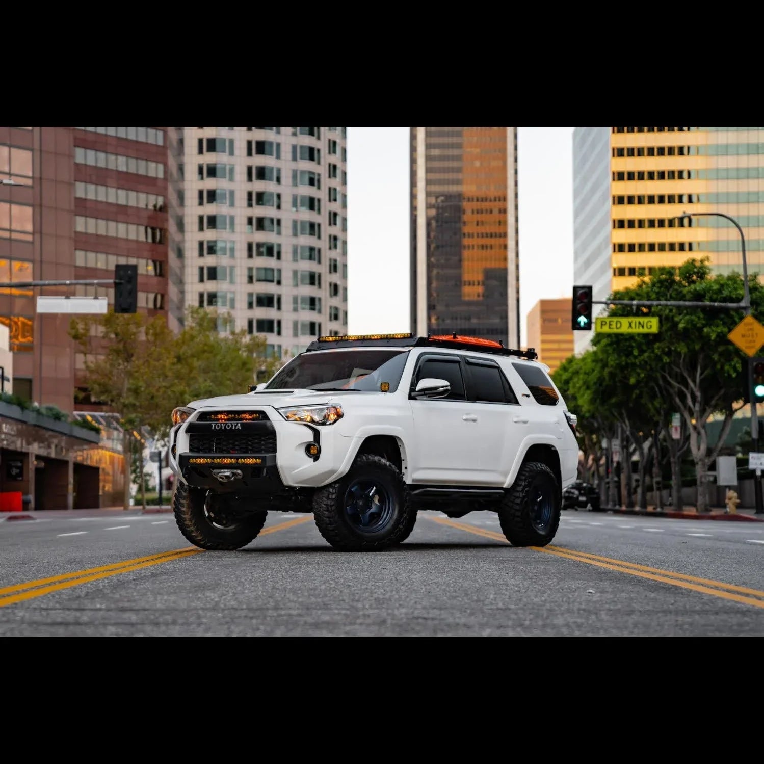 White Toyota 4Runner with off-road accessories parked on city street with tall buildings