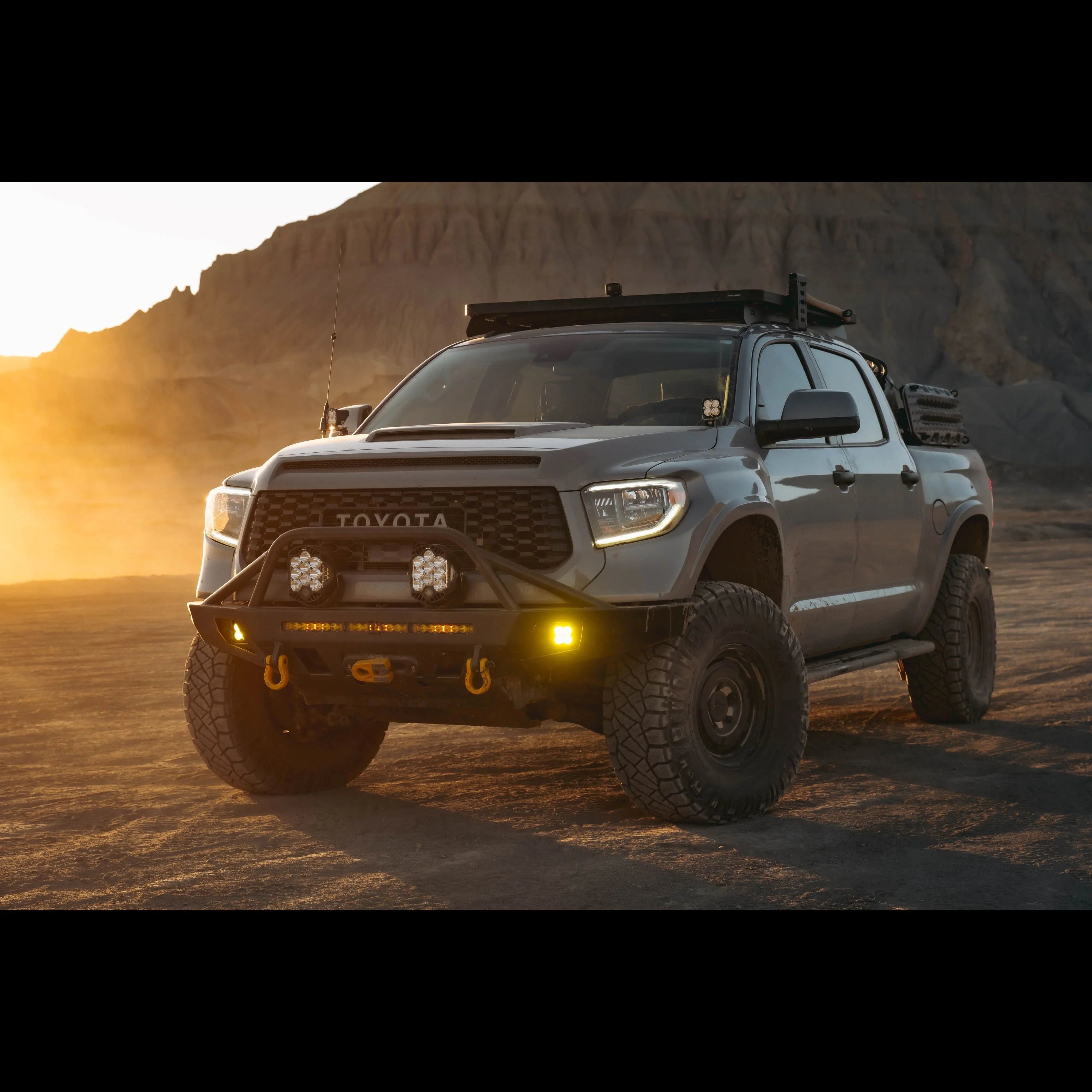 Lifted Toyota Tundra with off-road bumper, roof rack, and rugged tires in desert at sunset