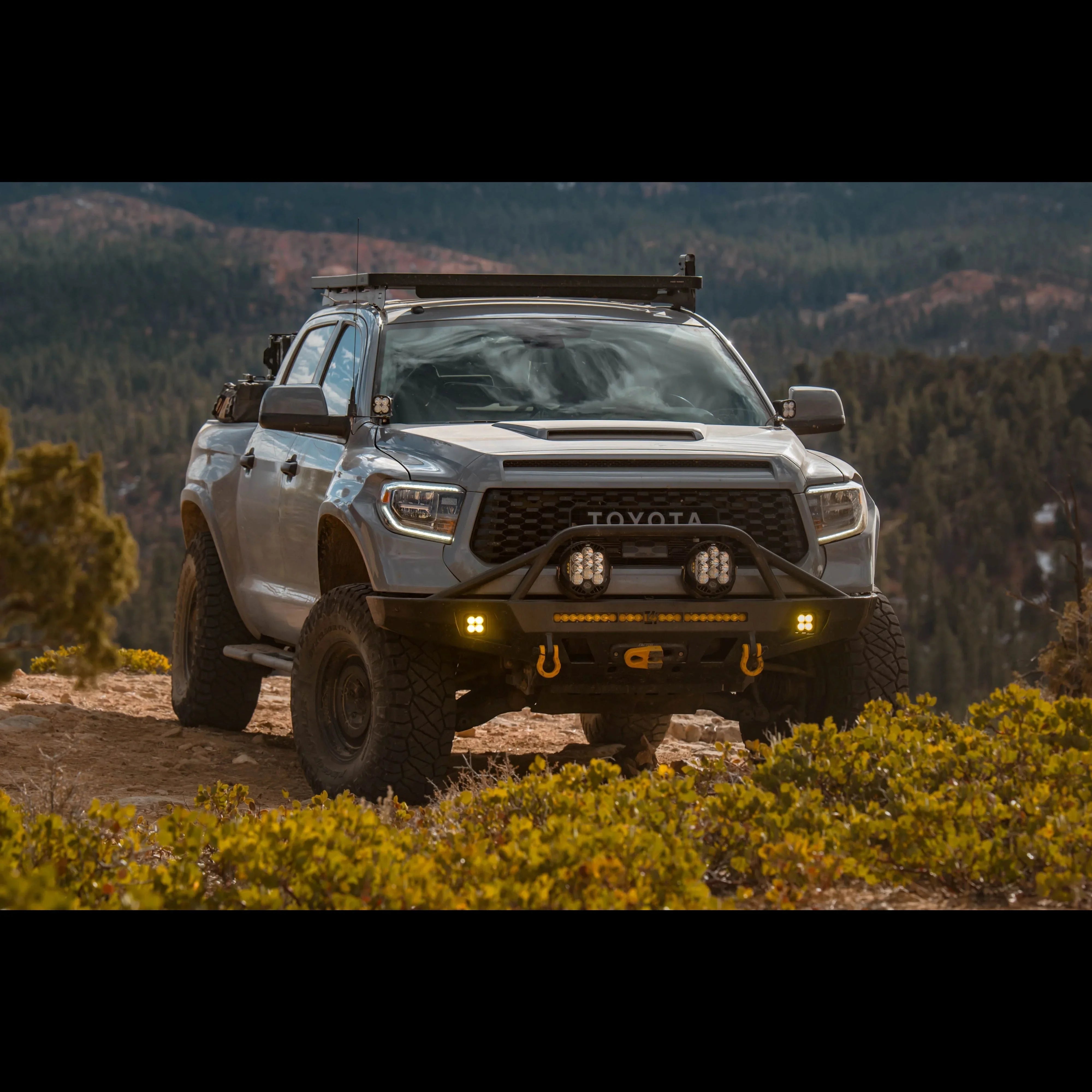 Toyota Tundra with off-road bumper, winch, roof rack, and LED lights on rugged mountain trail