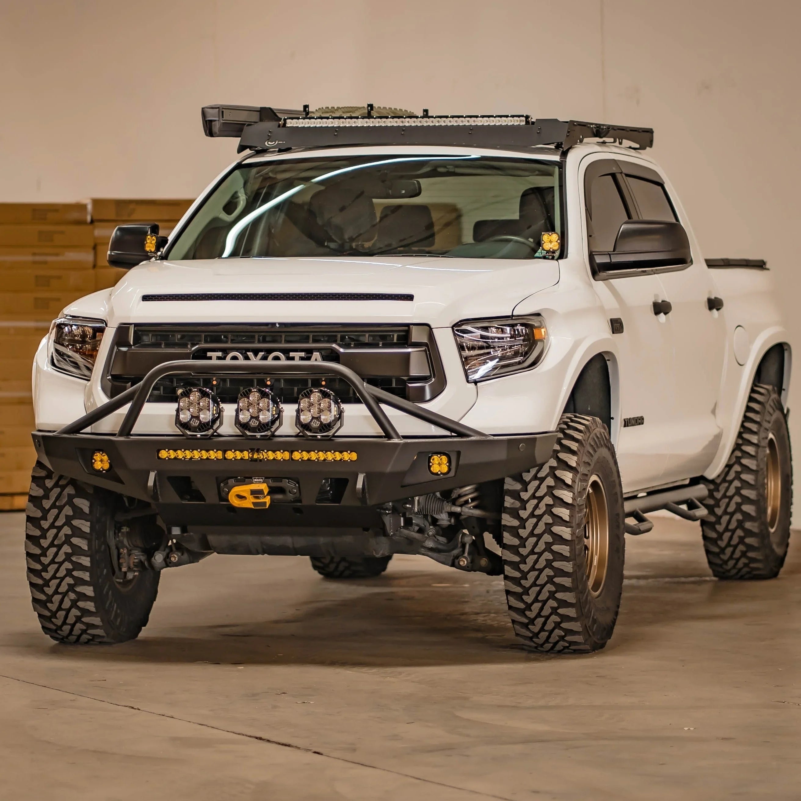 White Toyota Tundra with off-road bumper, LED lights, roof rack and all-terrain tires in garage