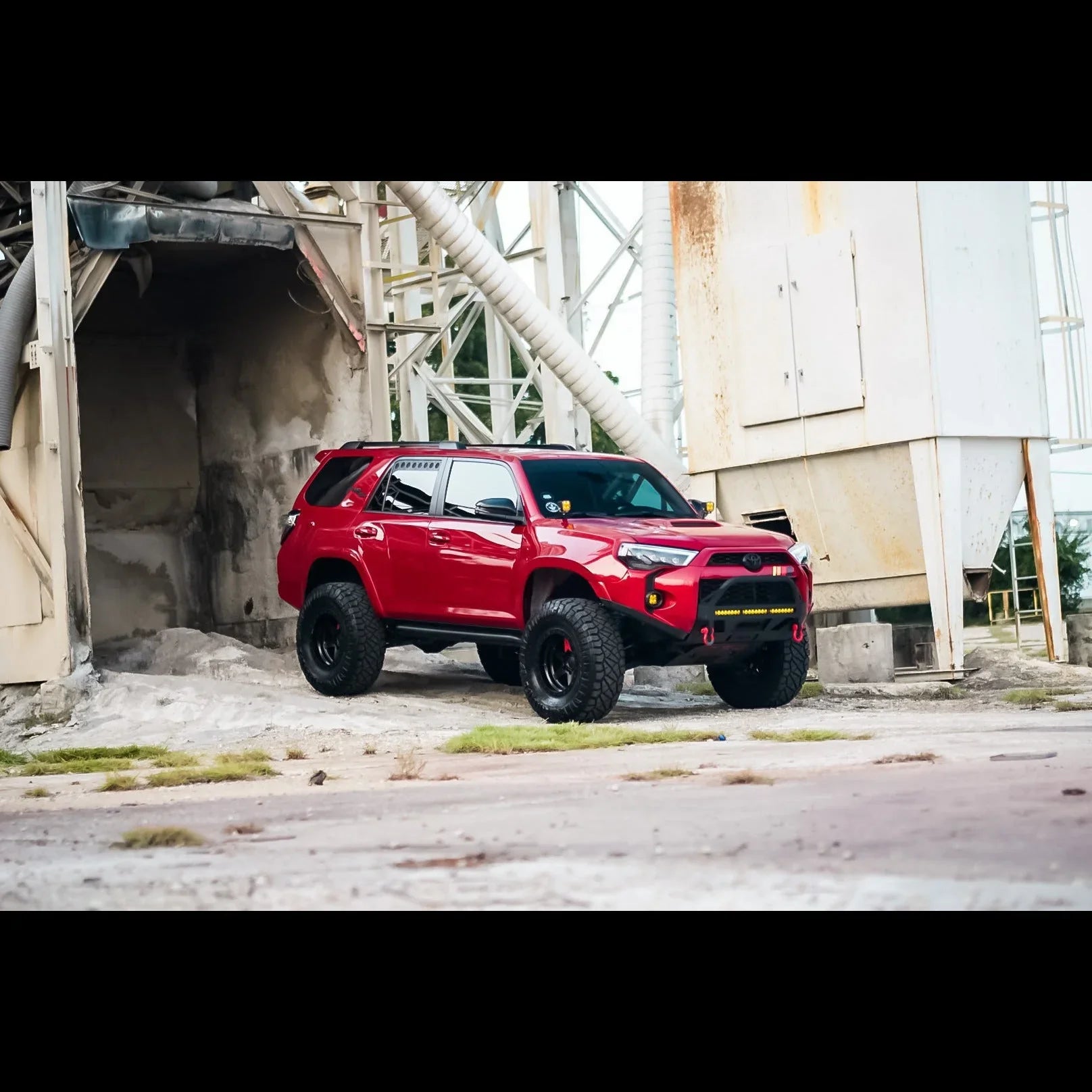 Lifted red Toyota 4Runner with off-road tires and accessories parked at industrial site