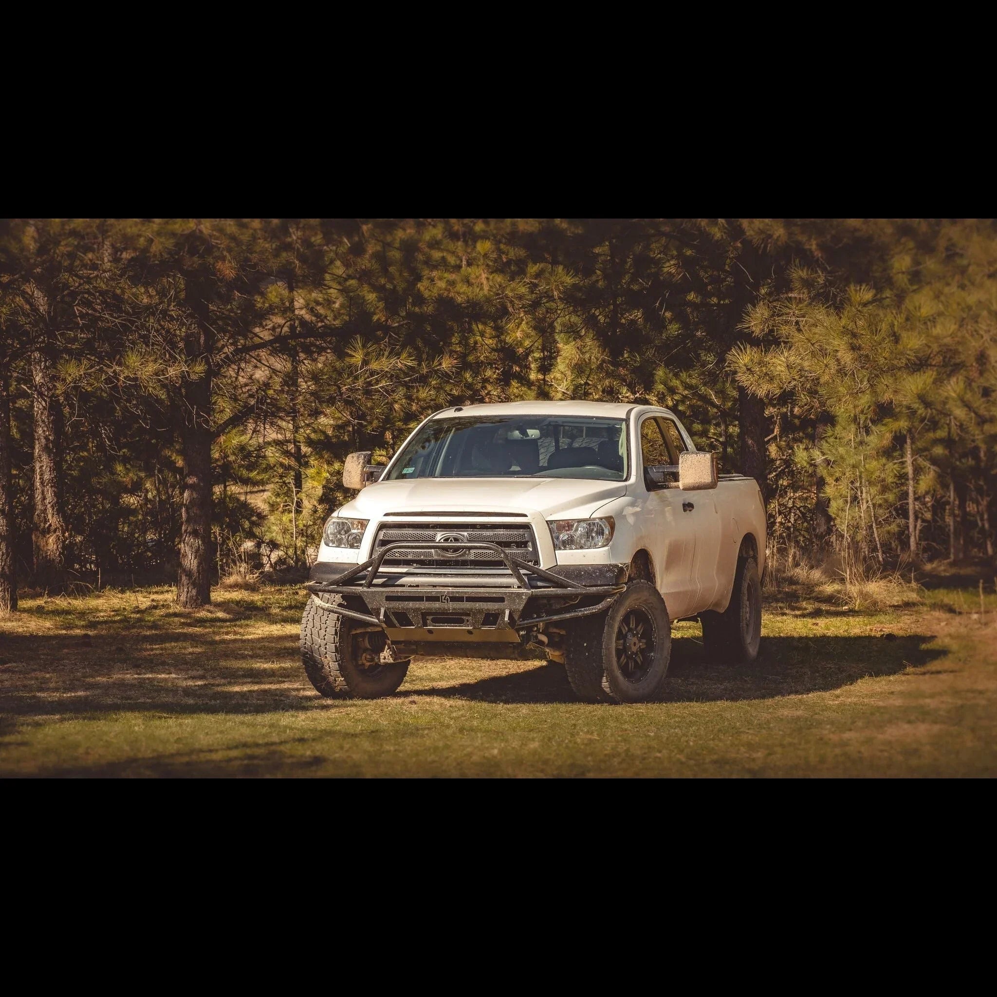 White Toyota Tundra with off-road bumper and large tires parked in forest clearing