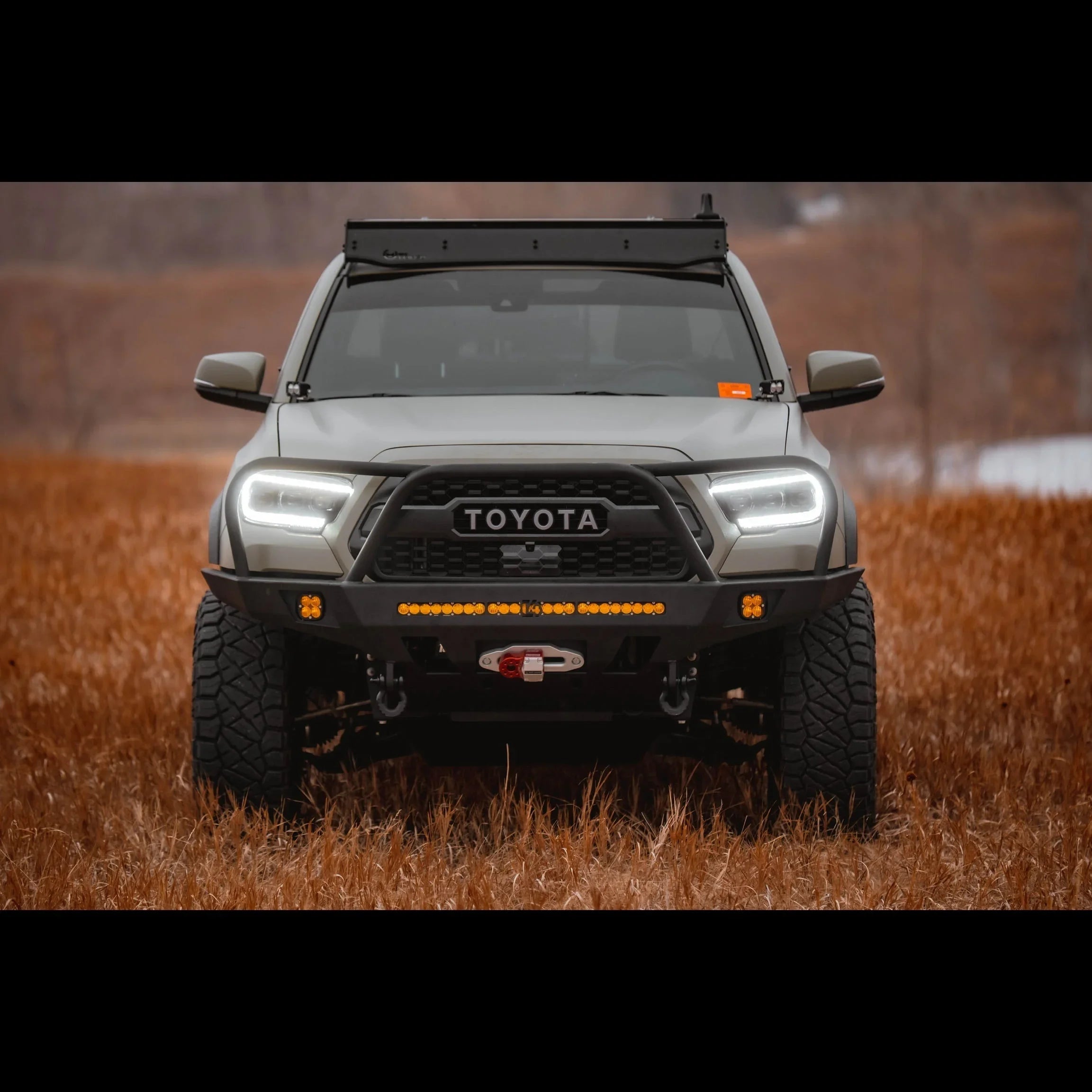 Toyota Tacoma with overland front bumper, LED lights, and off-road winch in a field