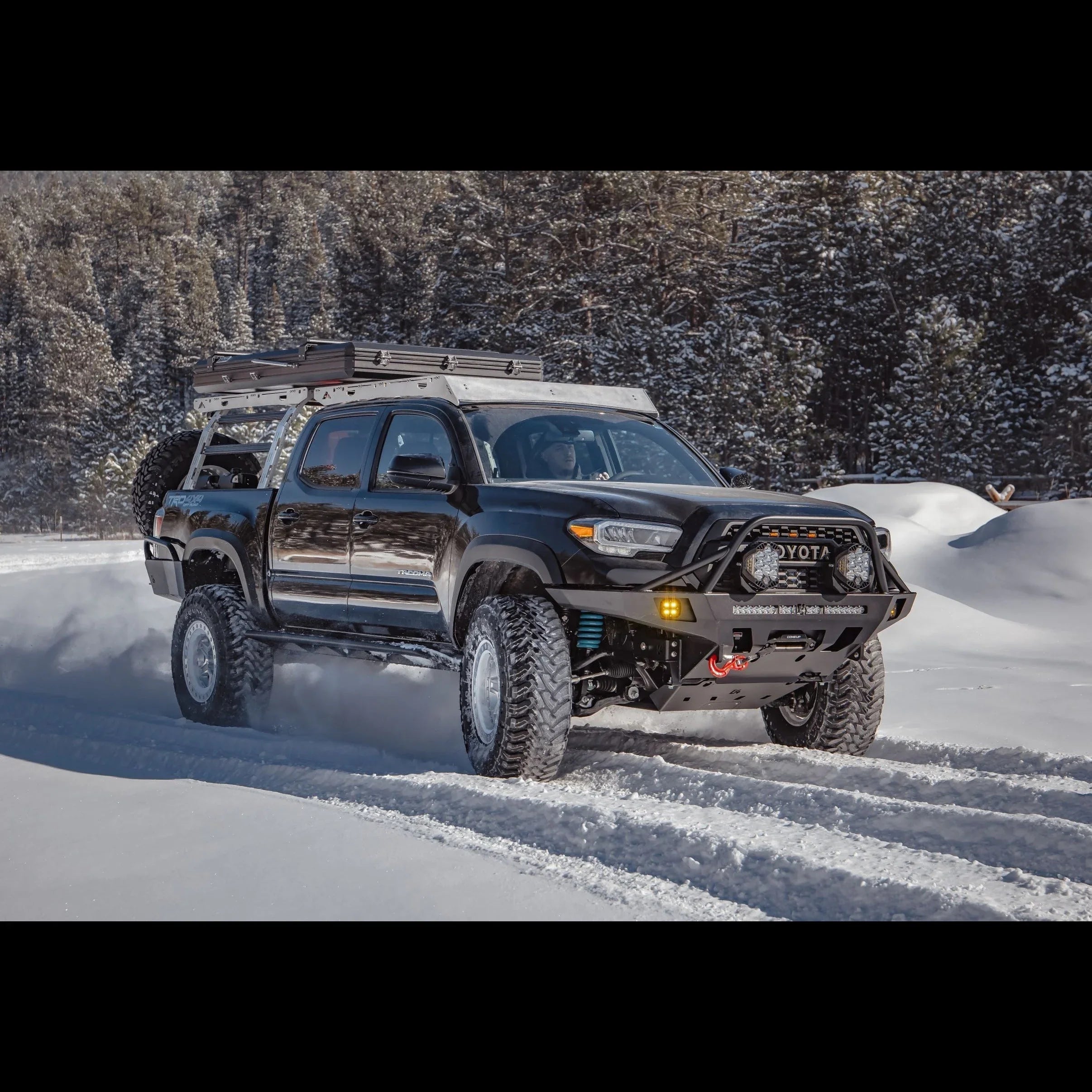 Toyota Tacoma with overland front bumper and roof rack driving in snowy forest