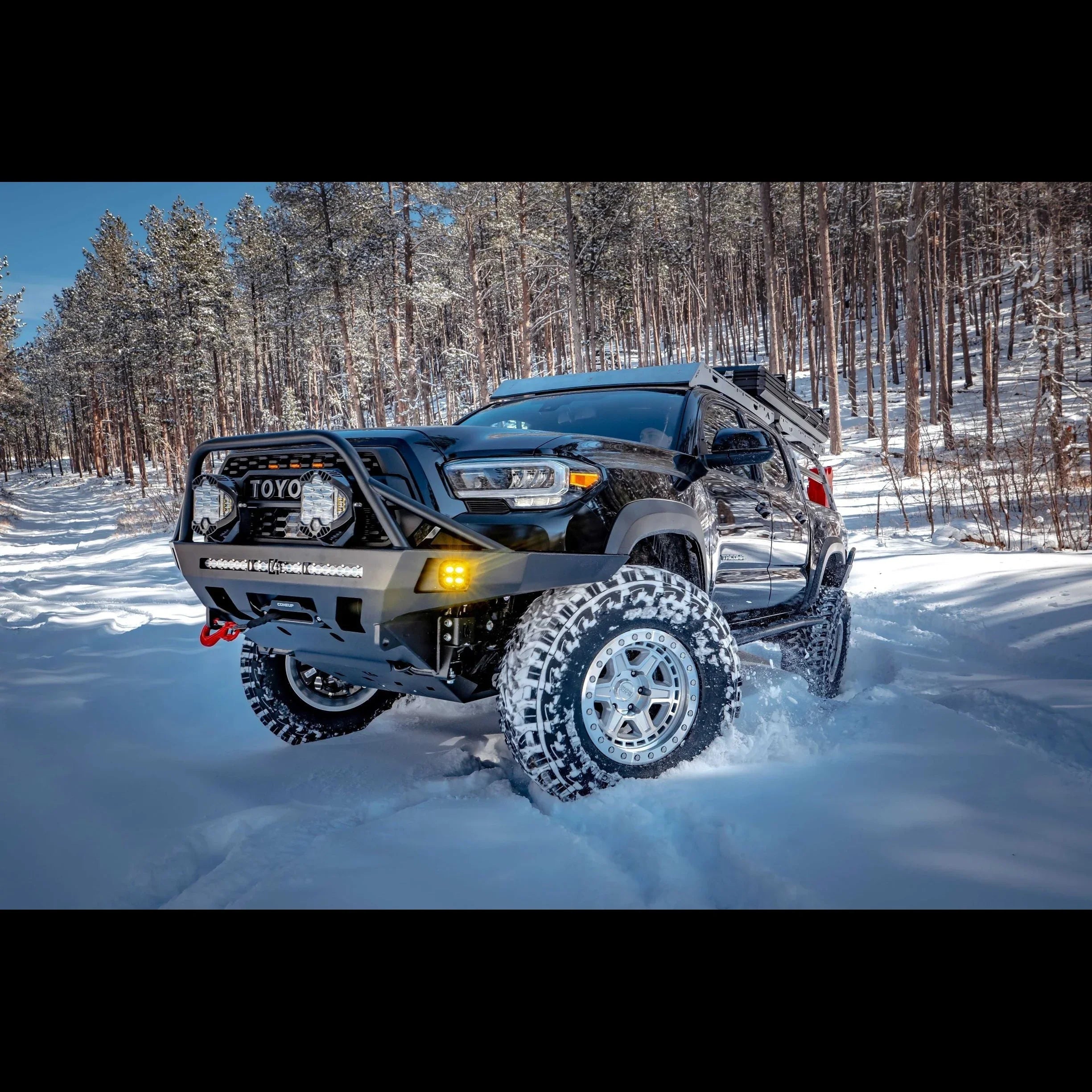 Toyota Tacoma with overland front bumper and off-road lights driving in snowy forest