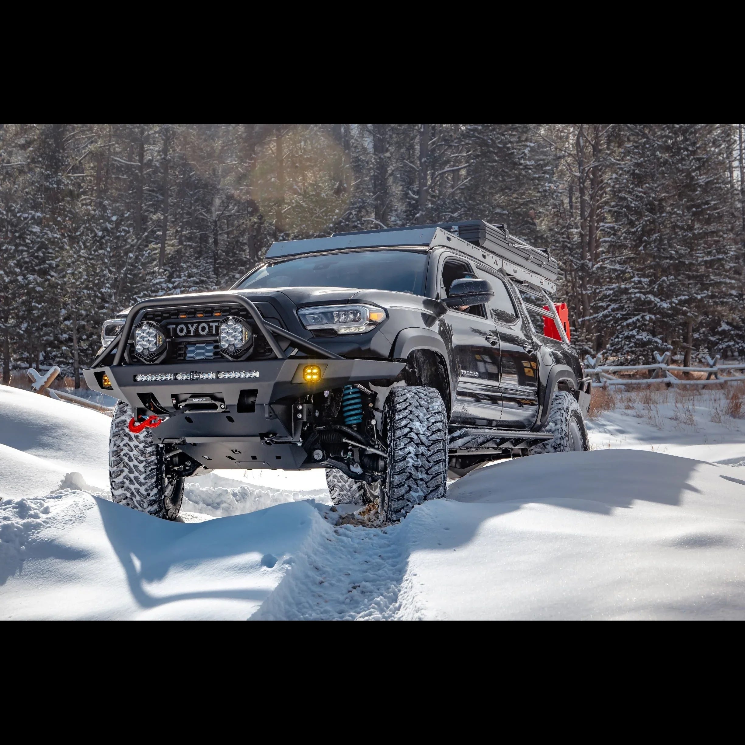 Toyota Tacoma with overland front bumper and off-road gear driving in snowy forest trail