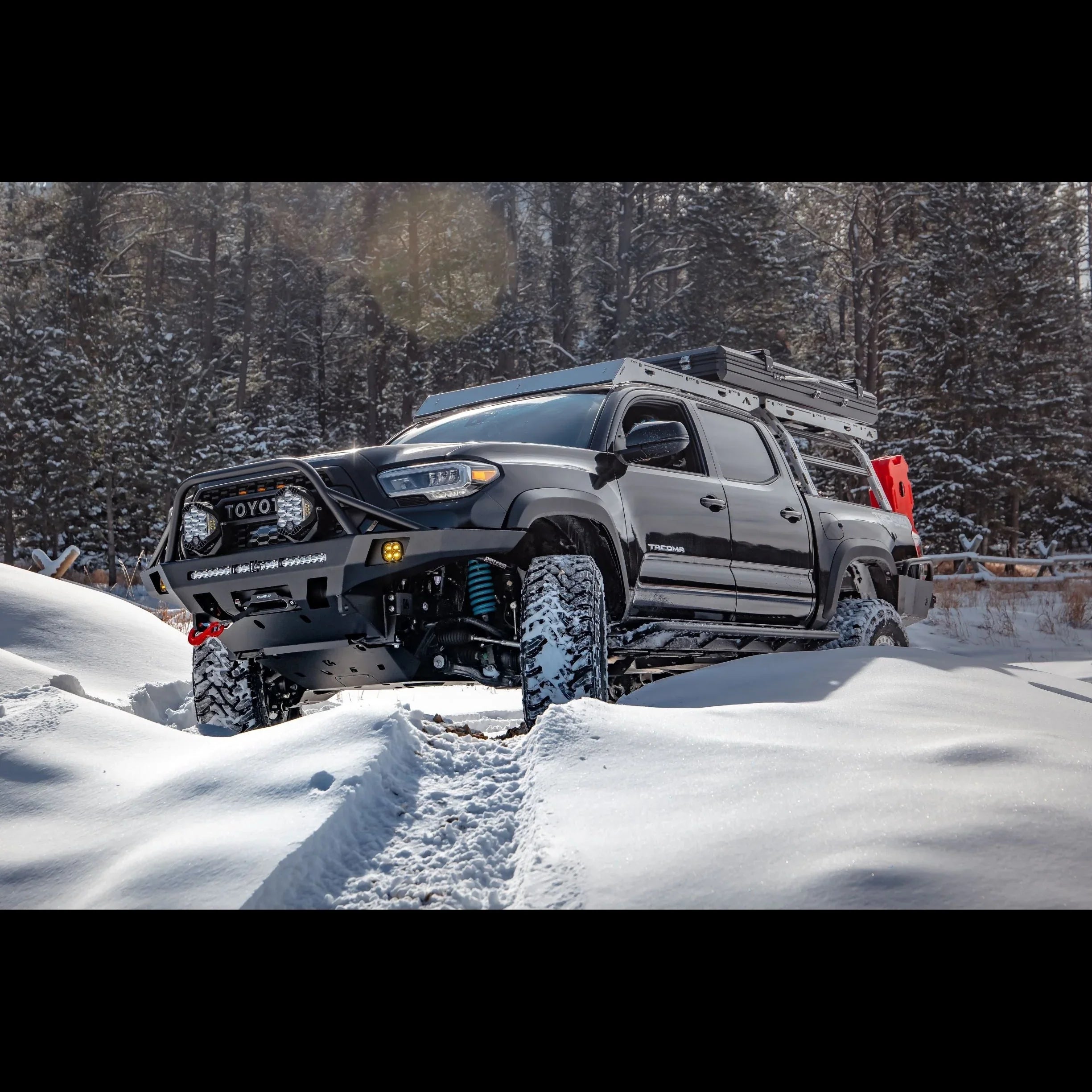 Toyota Tacoma with overland front bumper and roof rack driving through snowy forest