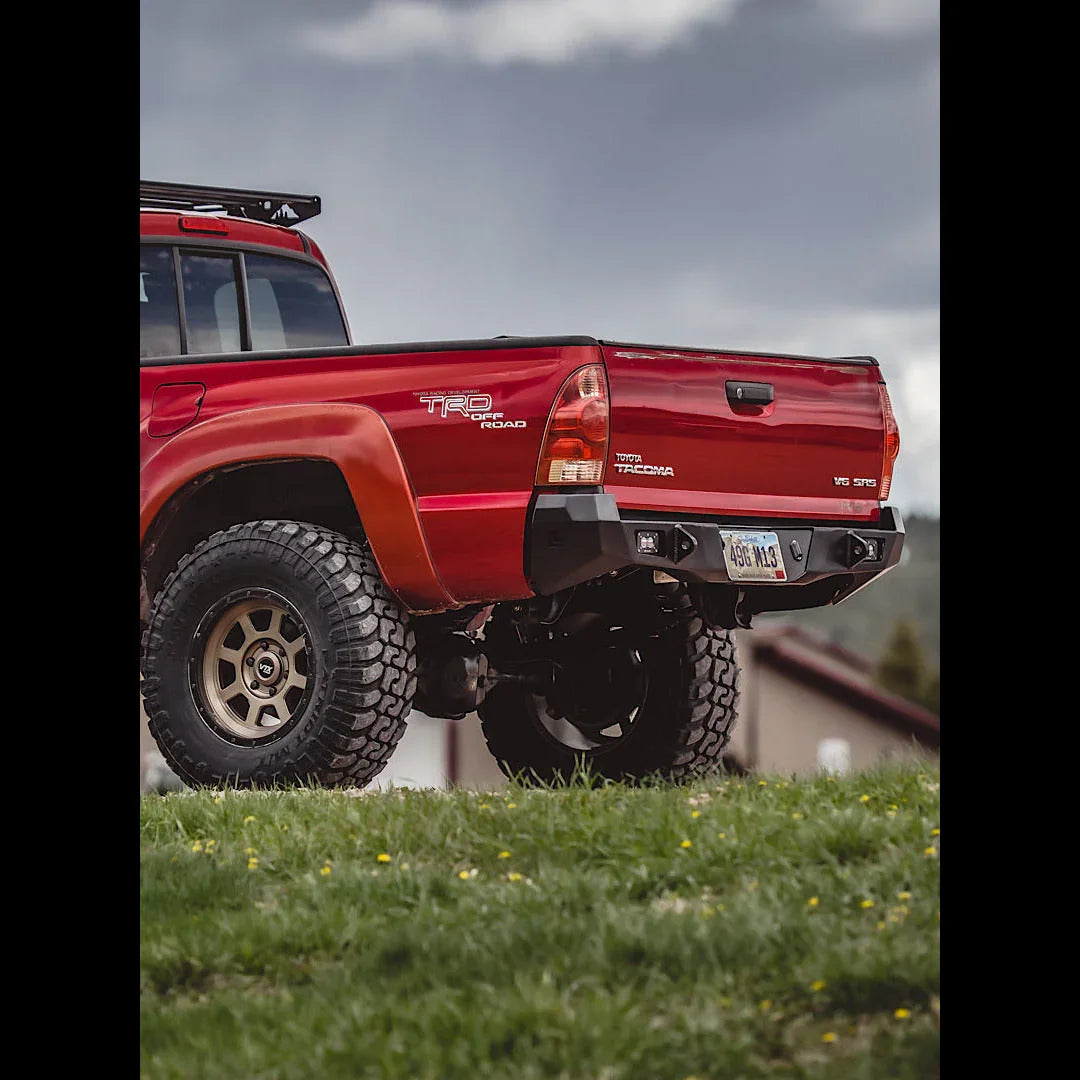 Off-road red Toyota Tacoma with overland rear bumper, parked on grassy terrain