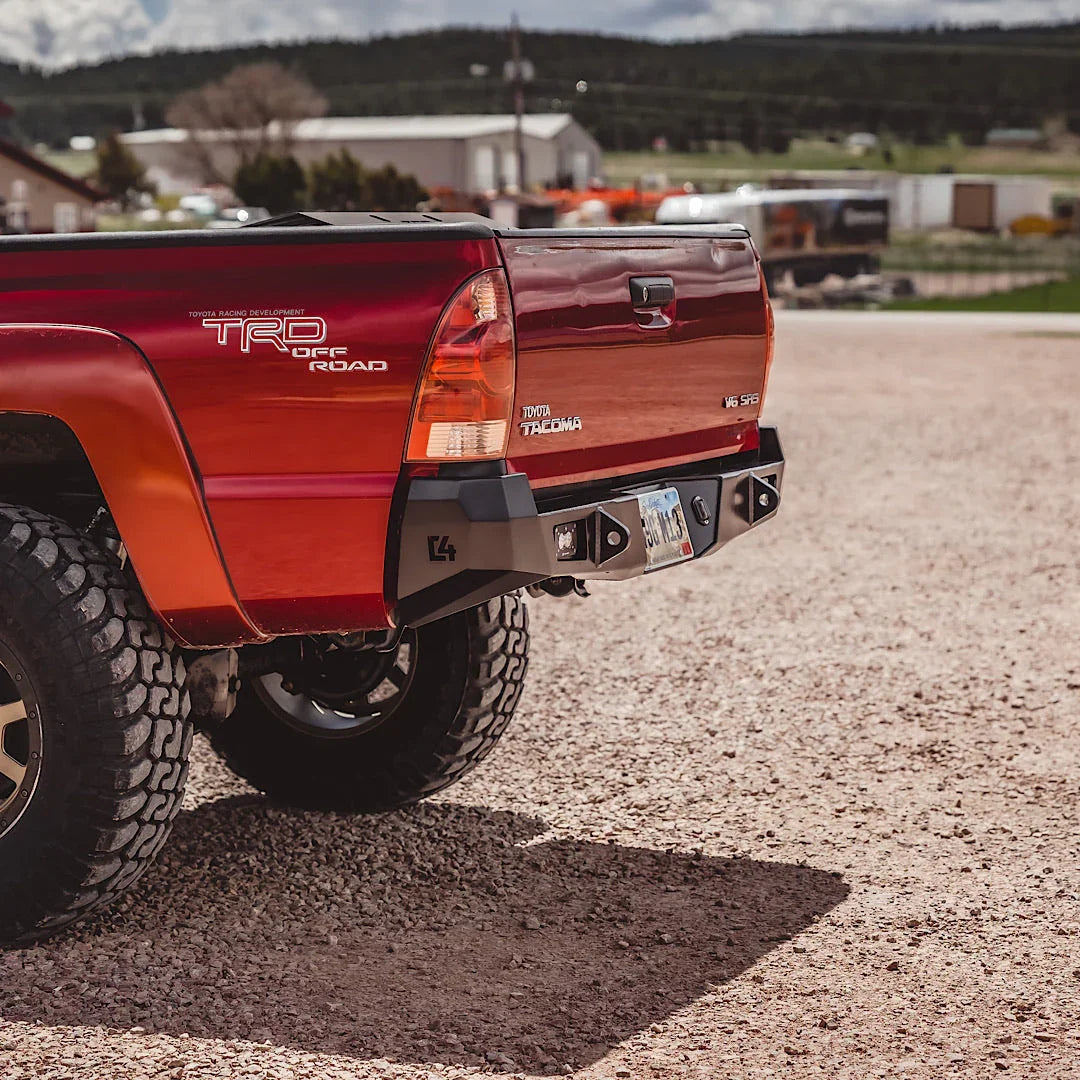 Toyota Tacoma with overland rear bumper, off-road tires, parked outdoors on gravel