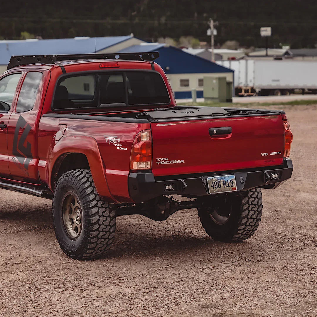 Red Toyota Tacoma with heavy-duty overland rear bumper parked on gravel
