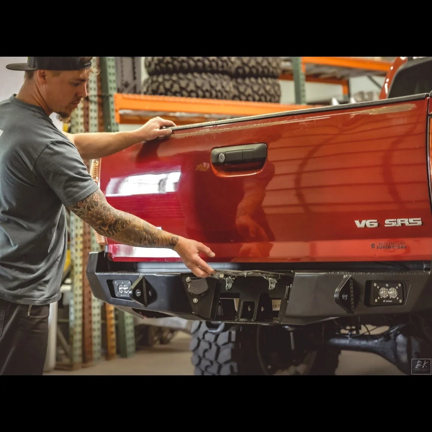 Man installing overland rear bumper on red Toyota Tacoma pickup truck