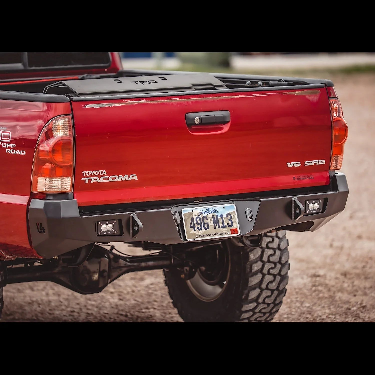 Aftermarket overland rear bumper on red Toyota Tacoma 2nd Gen truck, off-road setting