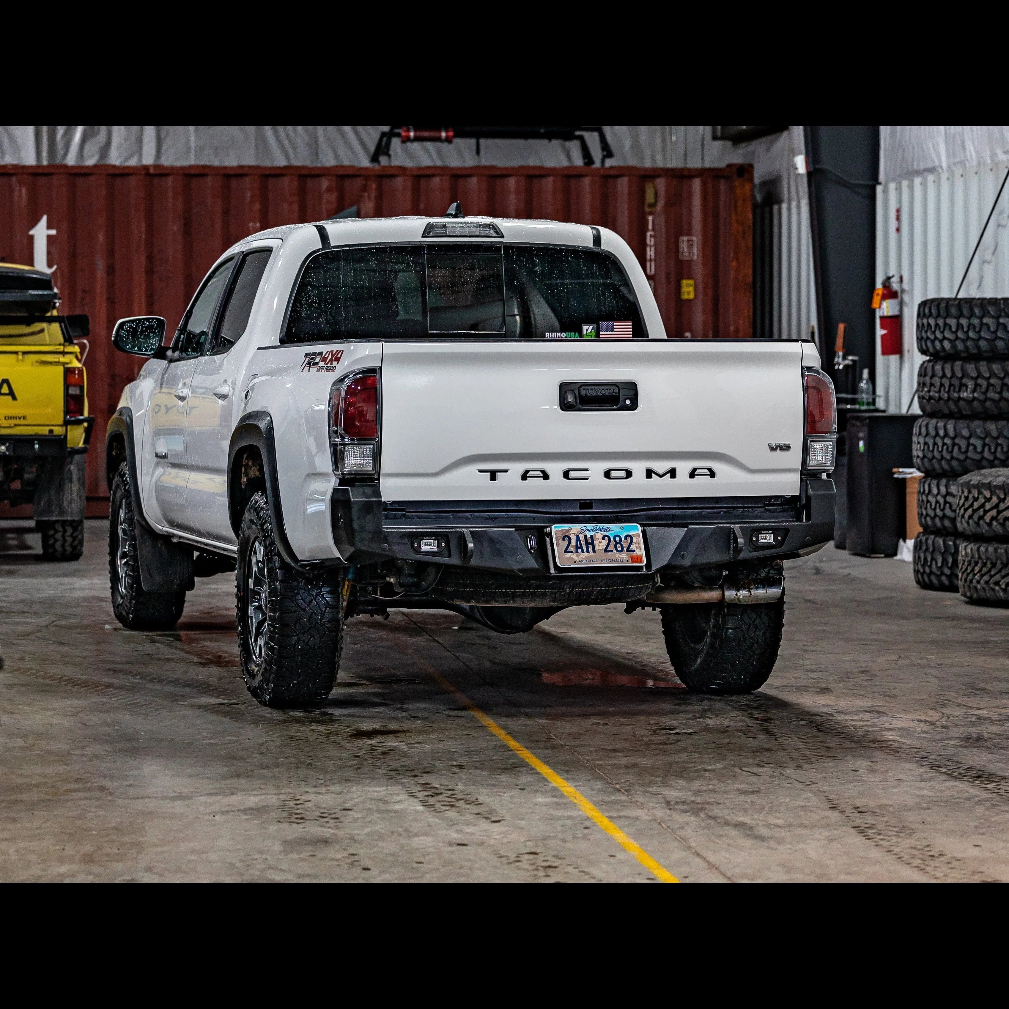 Toyota Tacoma 3rd Gen with overland rear bumper in a garage, off-road tires visible