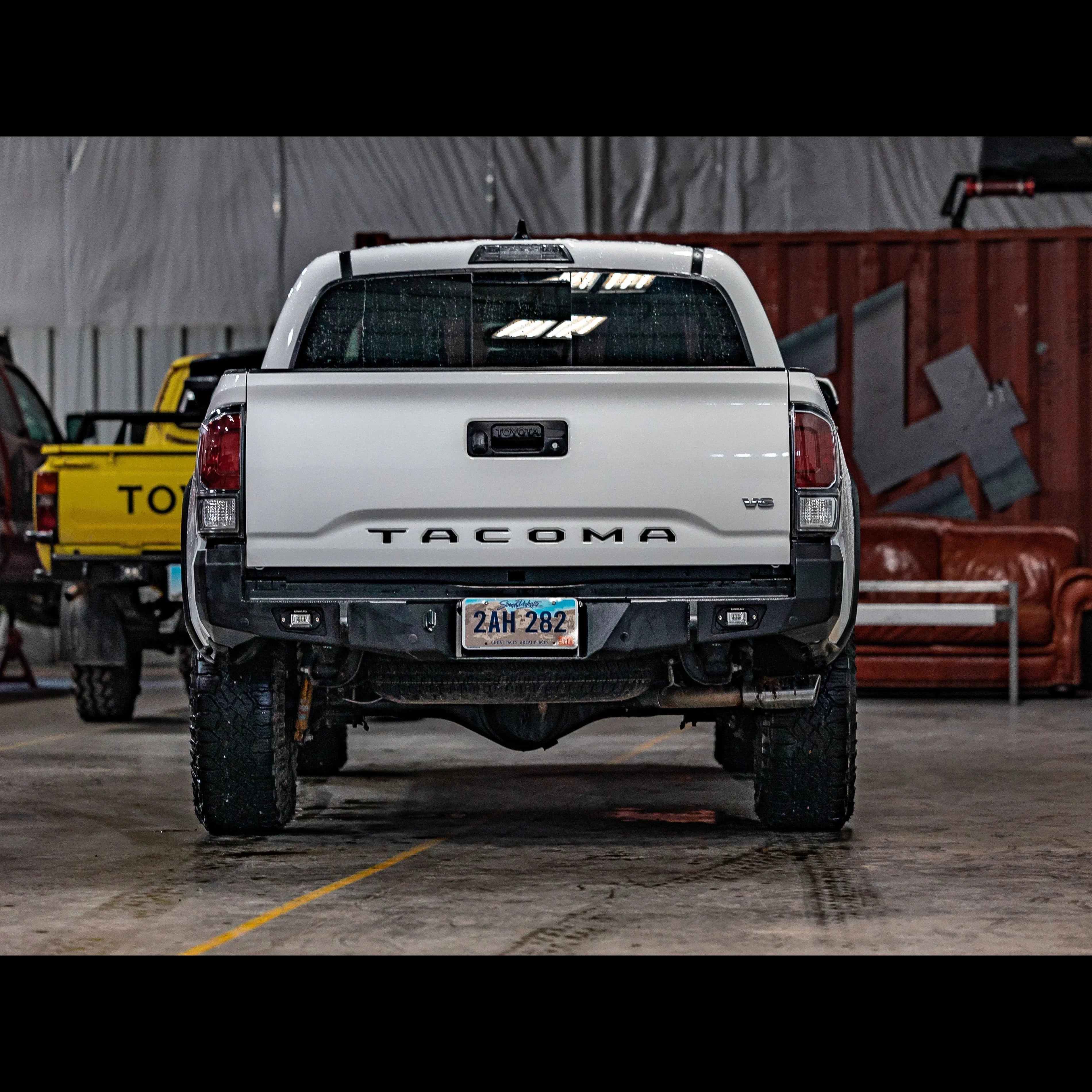 Rear view of white Toyota Tacoma with overland rear bumper in a garage setting