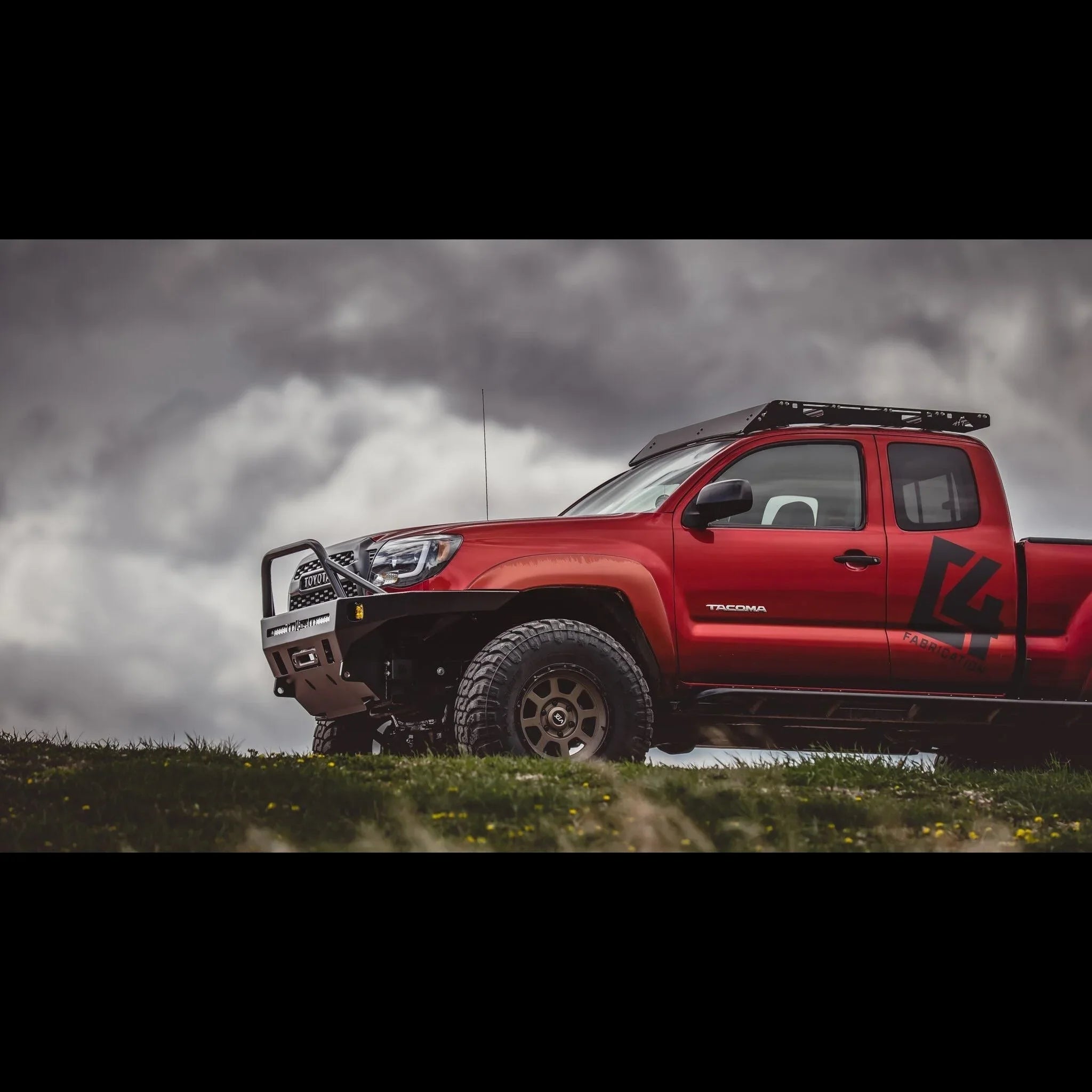 Red Toyota Tacoma with overland front bumper and roof rack outdoors, off-road setup