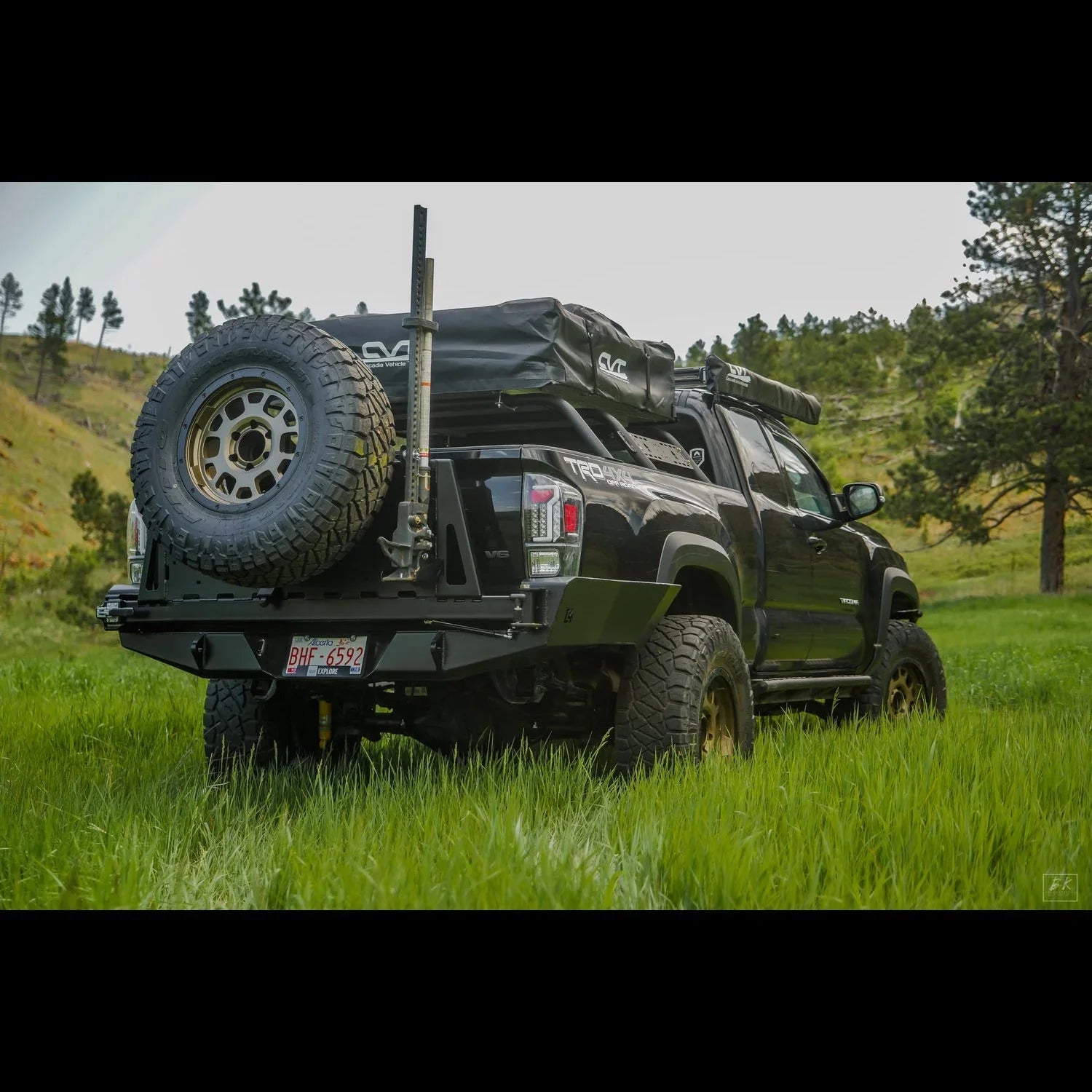 Toyota Tacoma with high clearance rear bumper, spare tire, off-road gear, parked on grass