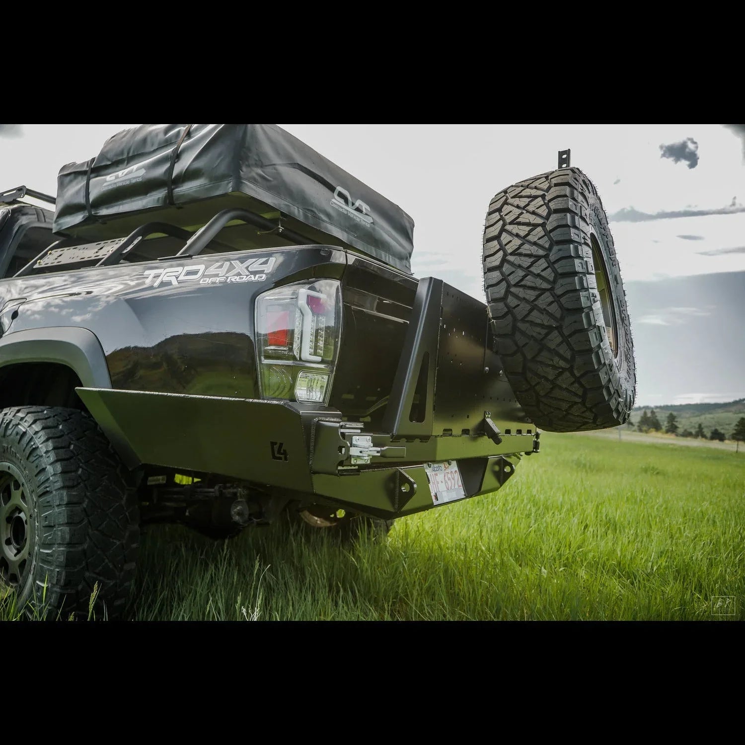 Toyota Tacoma with high clearance overland rear bumper and spare tire mount in grassy field