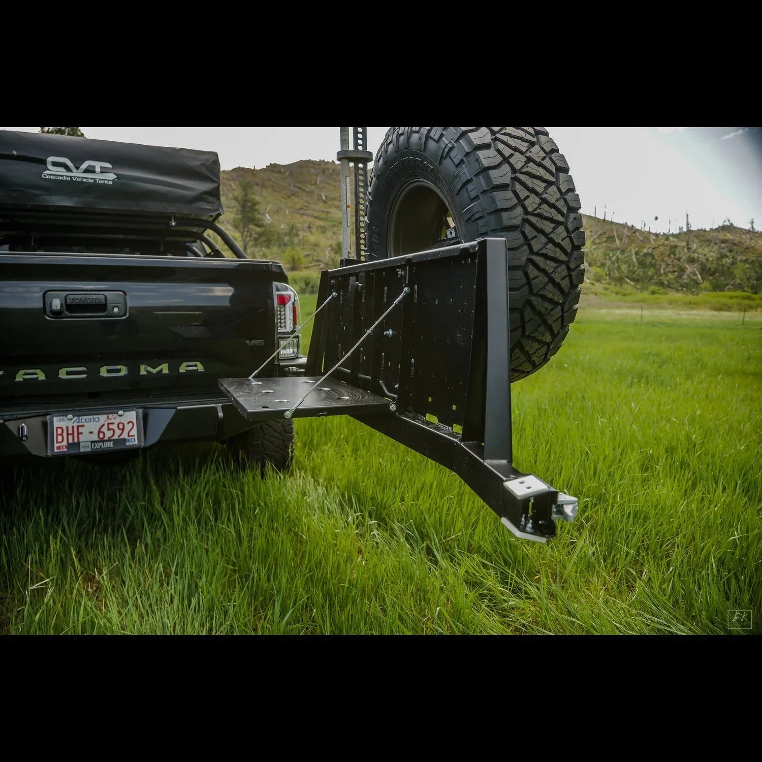 Toyota Tacoma with overland rear bumper and spare tire carrier in grassy outdoor setting