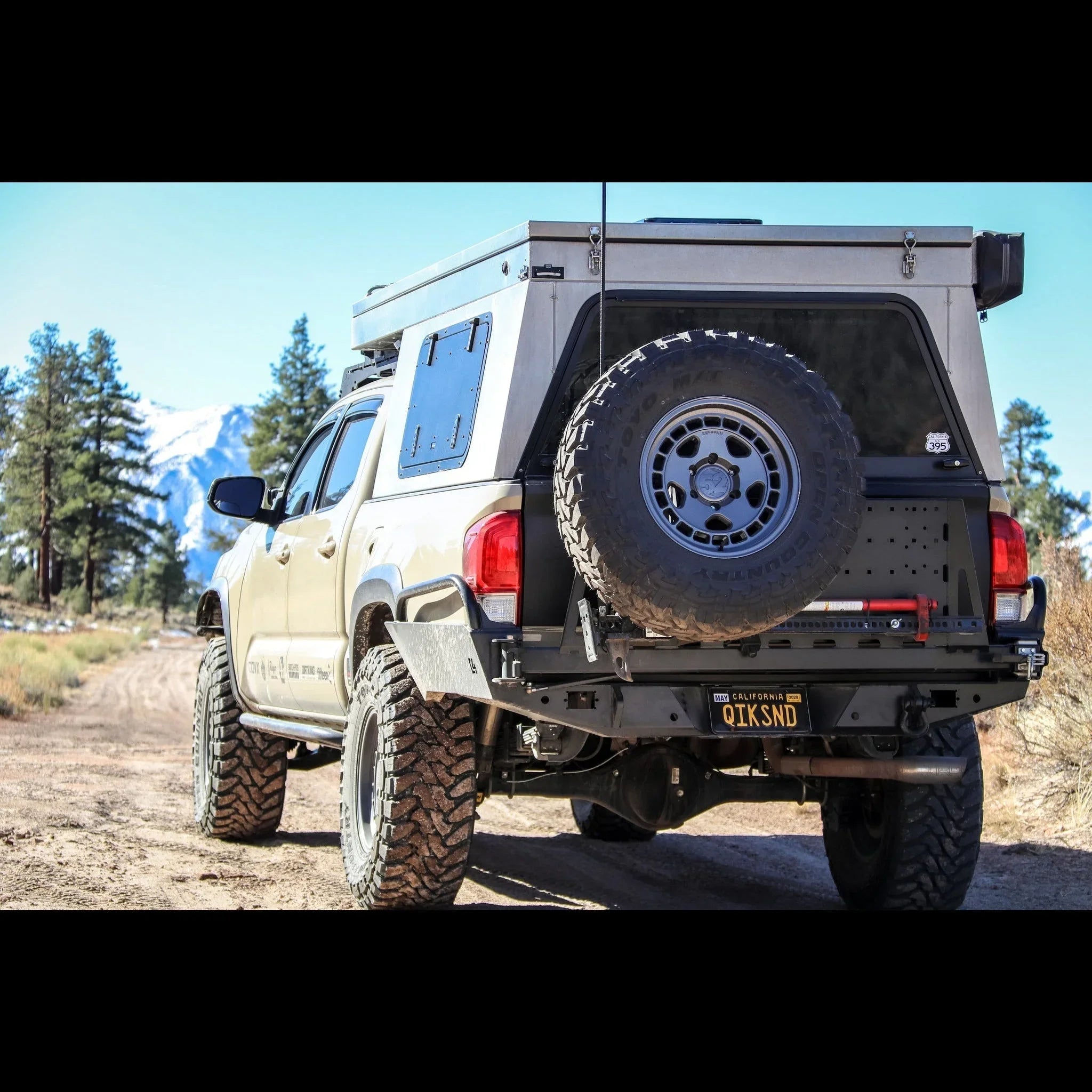 Toyota Tacoma with high clearance overland rear bumper, spare tire, and expedition gear outdoors