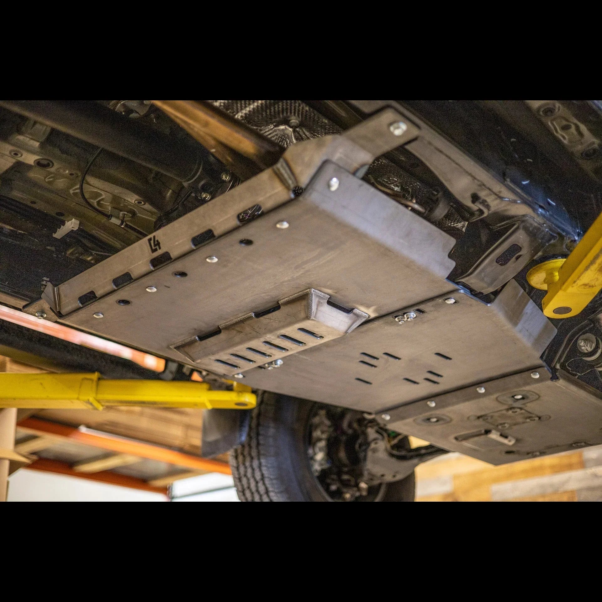 Heavy-duty steel rear skid plate installed under Toyota Tacoma, workshop setting