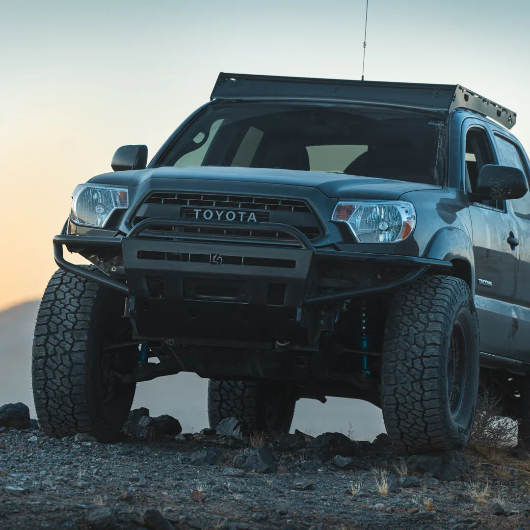 Toyota Tacoma with off-road front bumper and rugged tires on rocky terrain at sunset