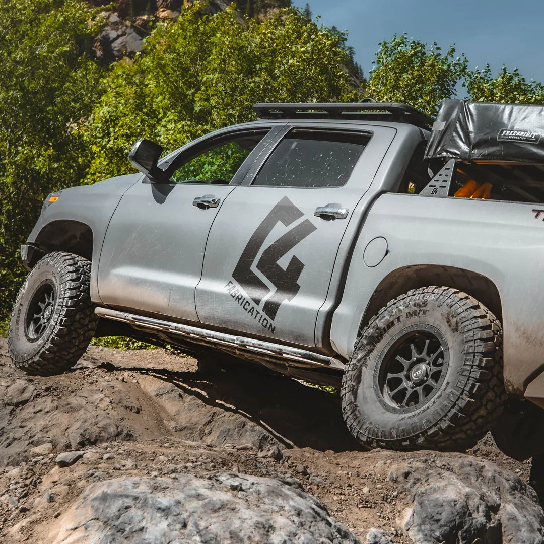 Toyota Tundra with rock sliders off-roading on rocky terrain, outdoor adventure gear shown
