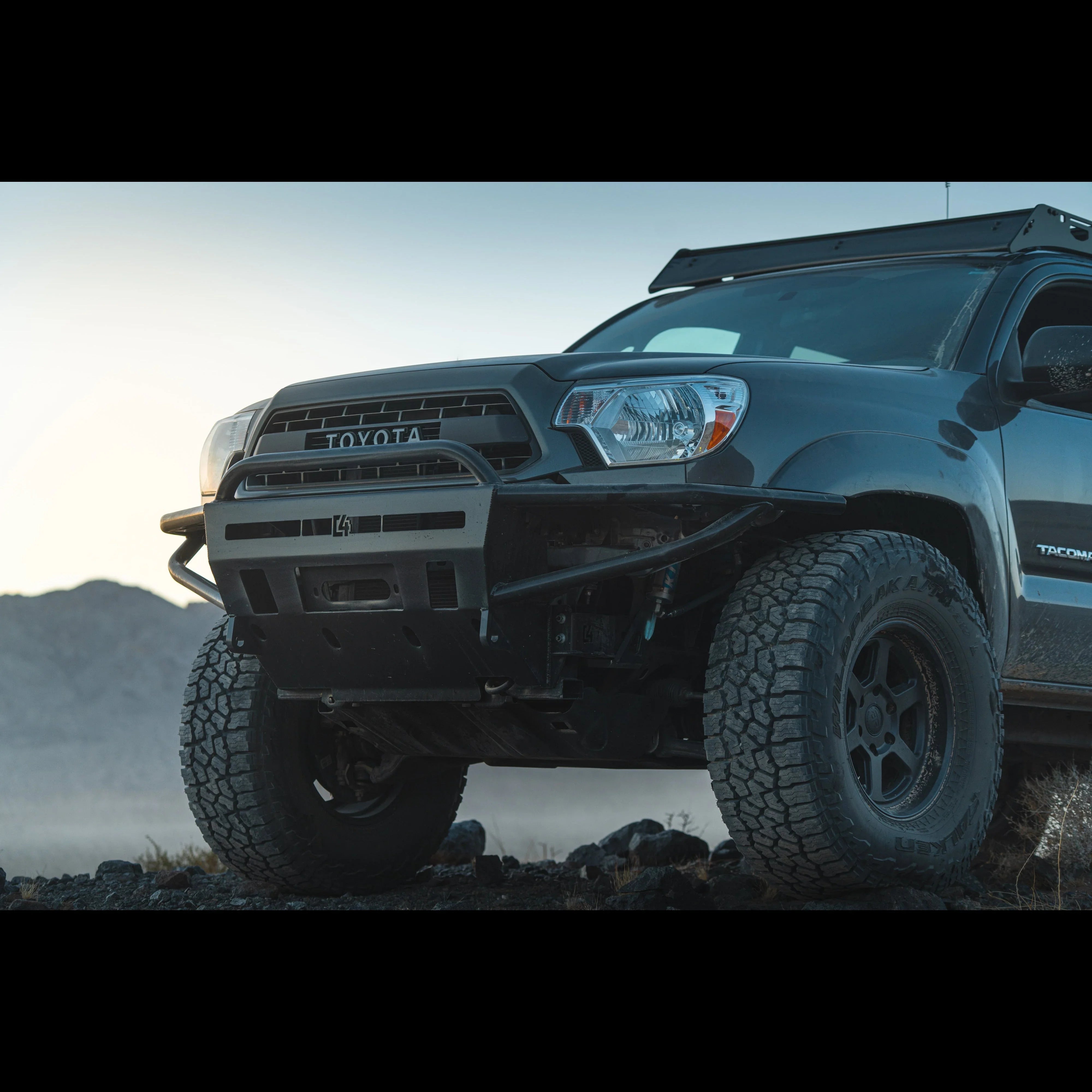 Toyota Tacoma front view with off-road bumper and all-terrain tires on rocky terrain