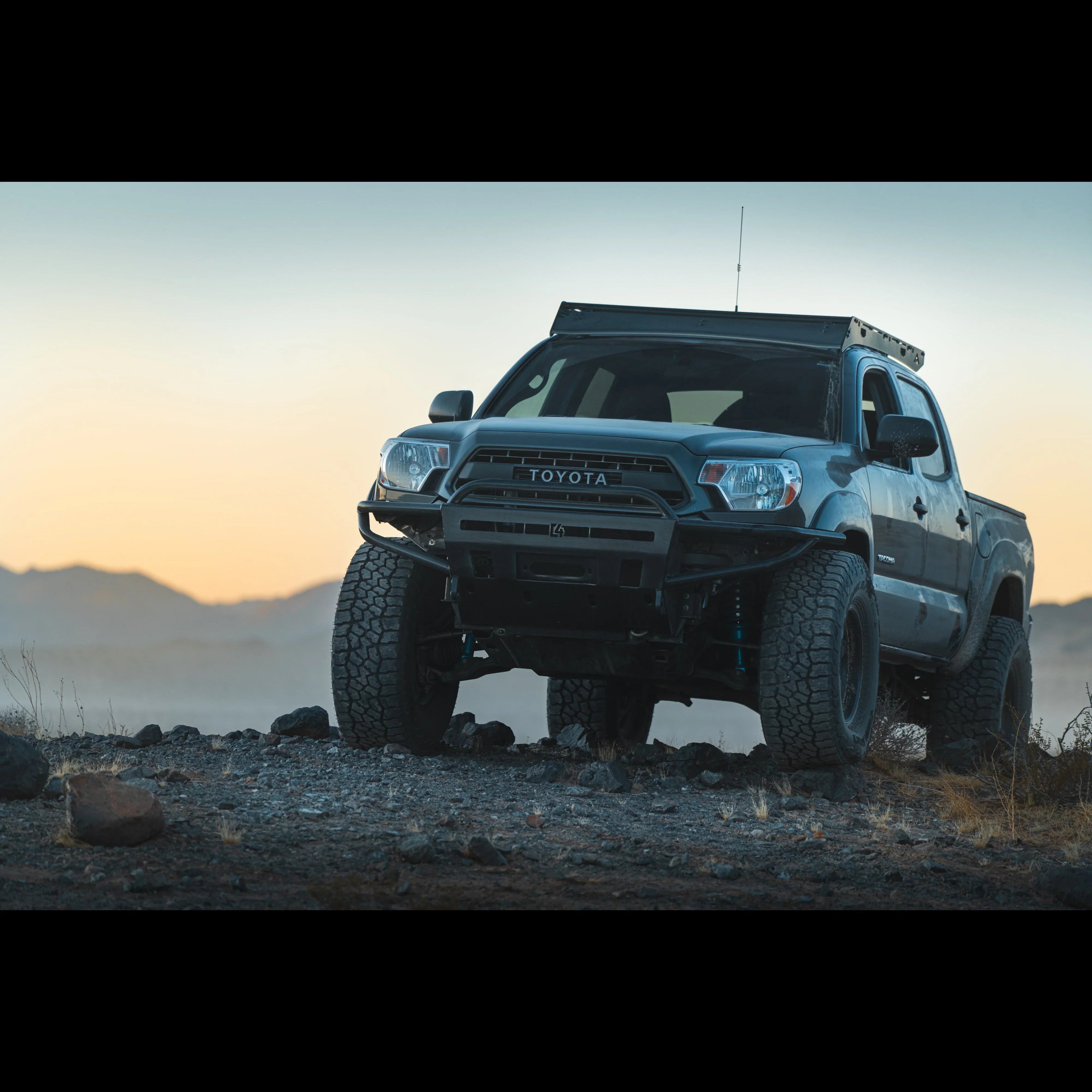 Lifted Toyota Tacoma with off-road tires and roof rack on rocky terrain at sunset