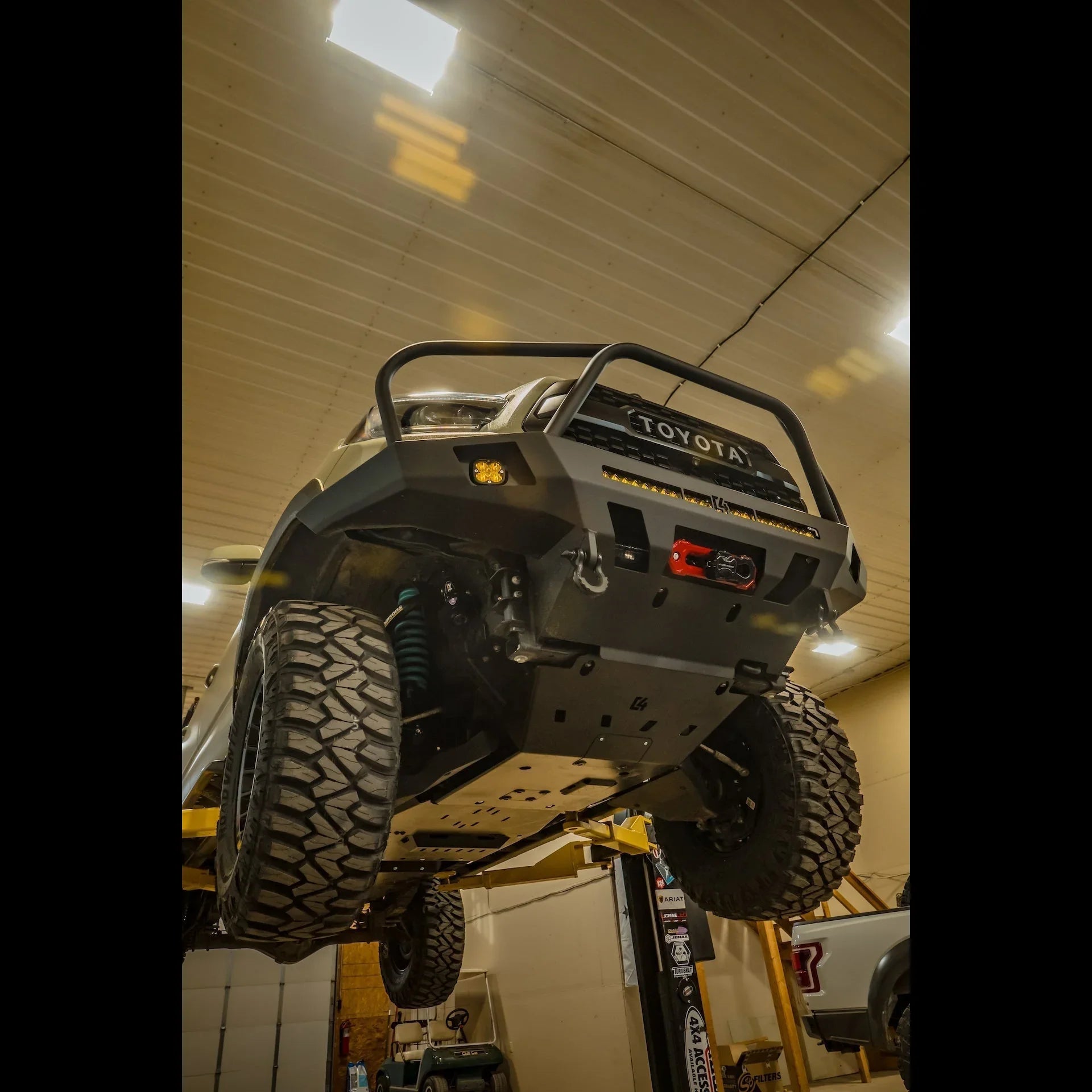 Toyota Tacoma with off-road bumper, lift kit, and rugged tires in garage workshop