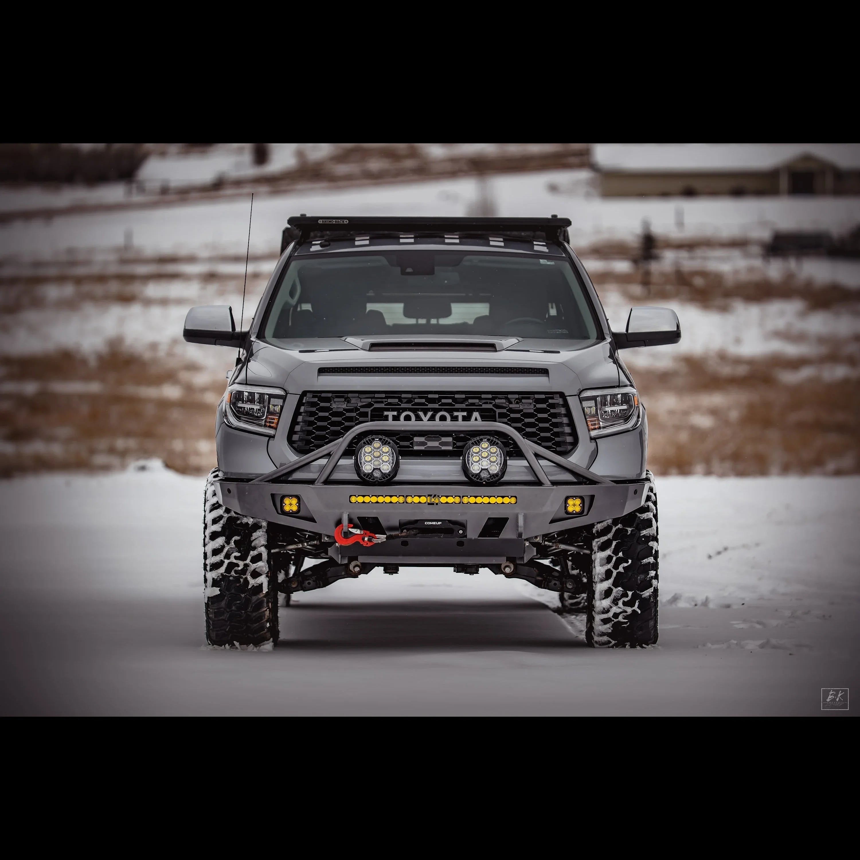 Front view of off-road Toyota Tundra with aftermarket bumper, driving lights, and snow tires in a snowy landscape