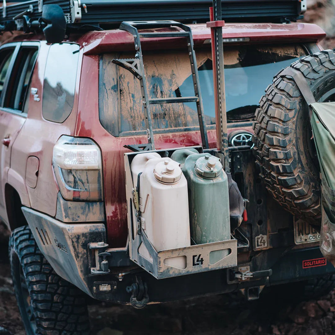Dual jerry can holder mounted on the rear of an off-road SUV with mud splatter and roof rack