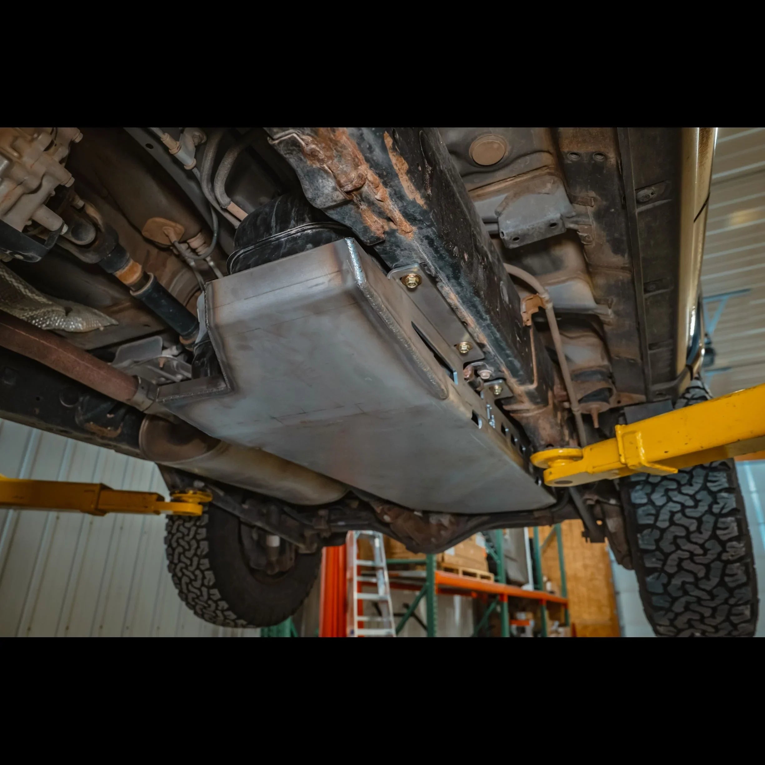 Heavy-duty gas tank skid plate installed under off-road vehicle, lifted in a workshop