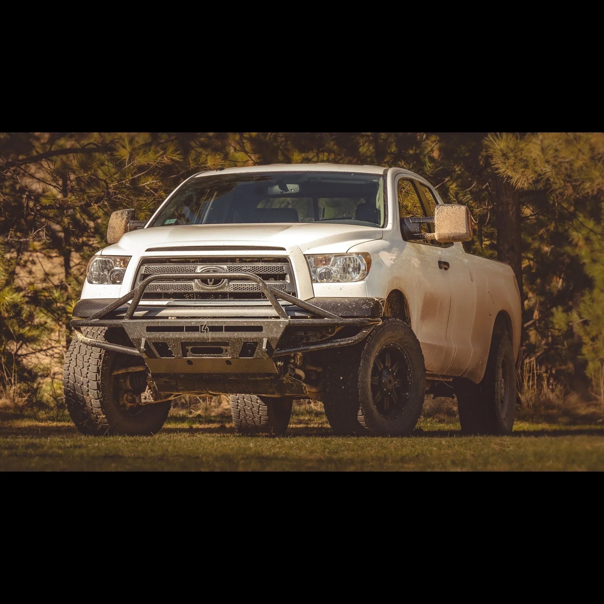 White Toyota Tundra with off-road front bumper, mud splashes, parked in outdoor setting