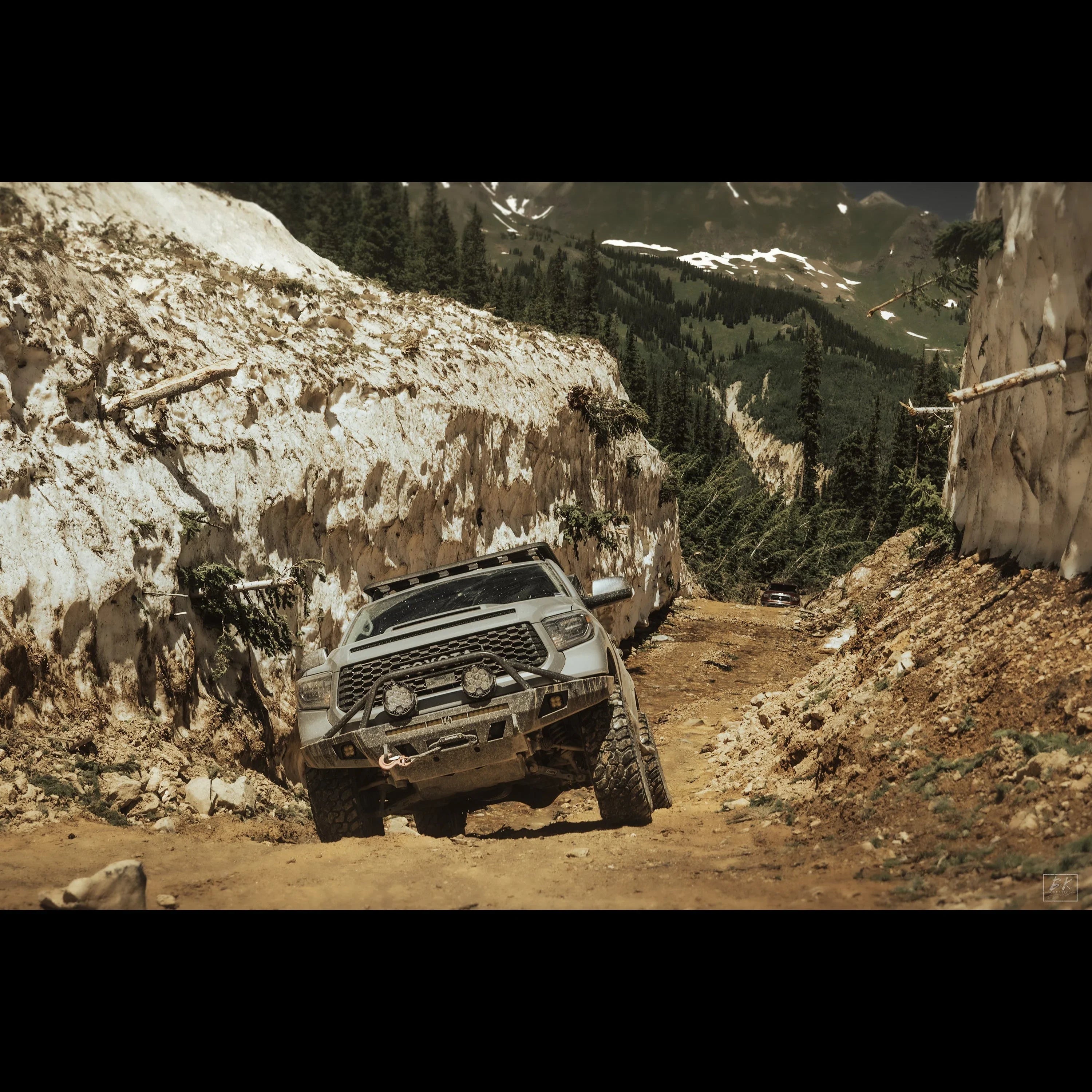 Toyota Tacoma off-road overlanding through rugged mountain trail with snow banks